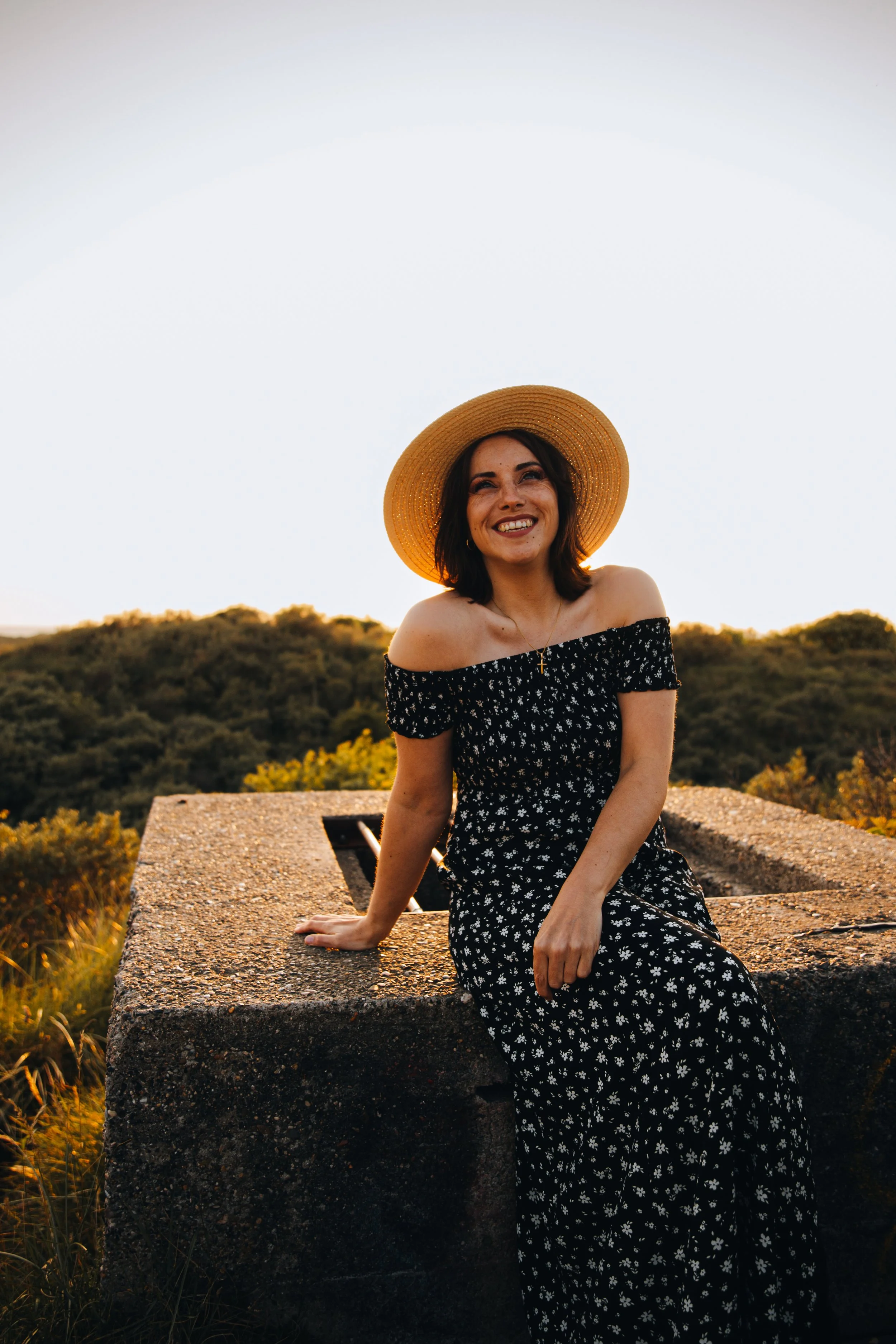 lachend-portret-van-jonge-vrouw-met-hoed-en-jurk-tijdens-golden-hour.jpg