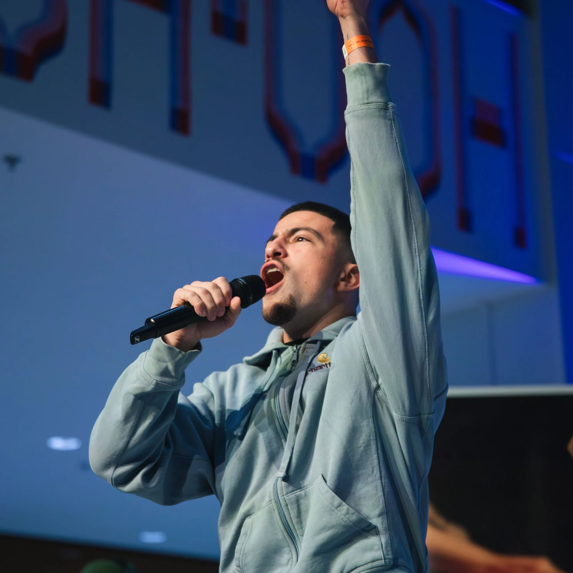 Man die spreekt in een microfoon met één hand omhoog.