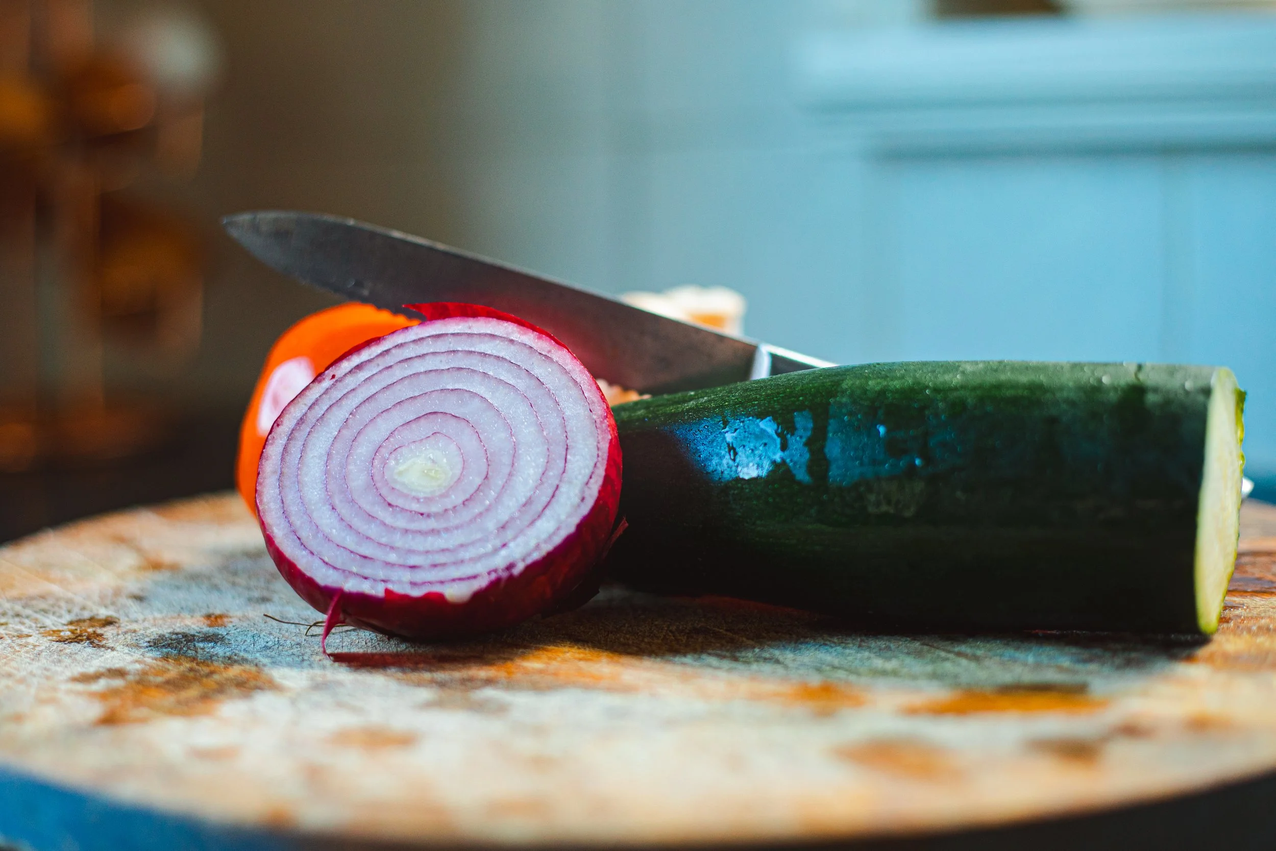 Detail van concentrische rode ui ringen, een courgette, tomaat en een scherp mes op een houten plank. Een perfecte foto voor verse ingrediënten en koken.