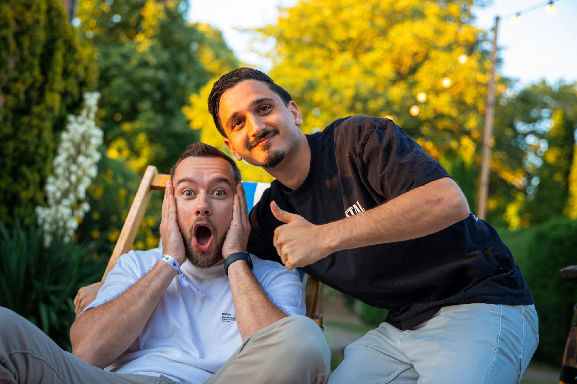 Twee collega's poseren spontaan en grappig voor de camera tijdens een zomerse bedrijfsborrel. De ene man kijkt met zijn handen op zijn wangen overdreven geschokt, terwijl de ander lachend een duim omhoog steekt. Pure sfeerfotografie door SteefClicks