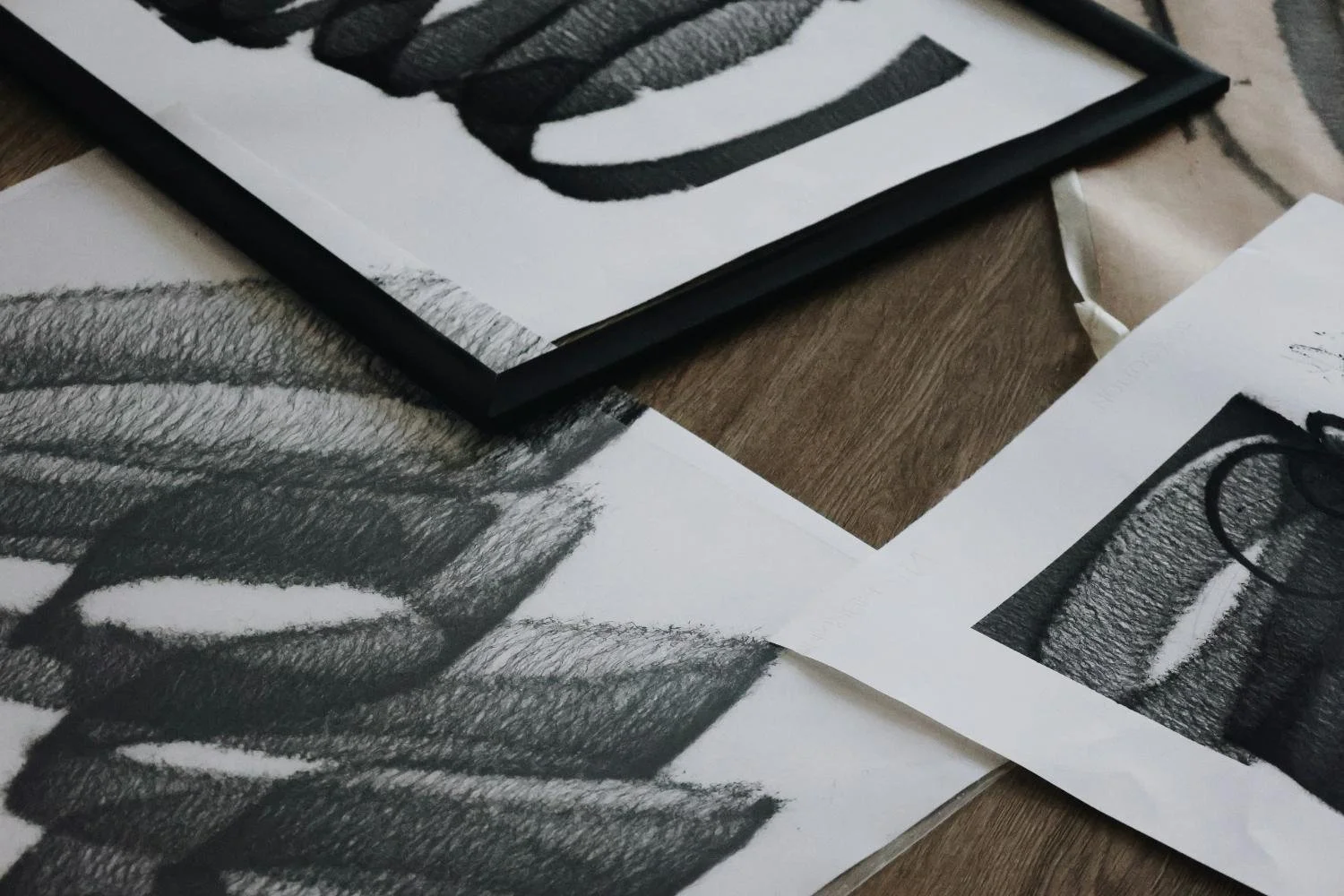 Black-and-white abstract artwork and sketches on paper, with a framed piece on a wooden surface.