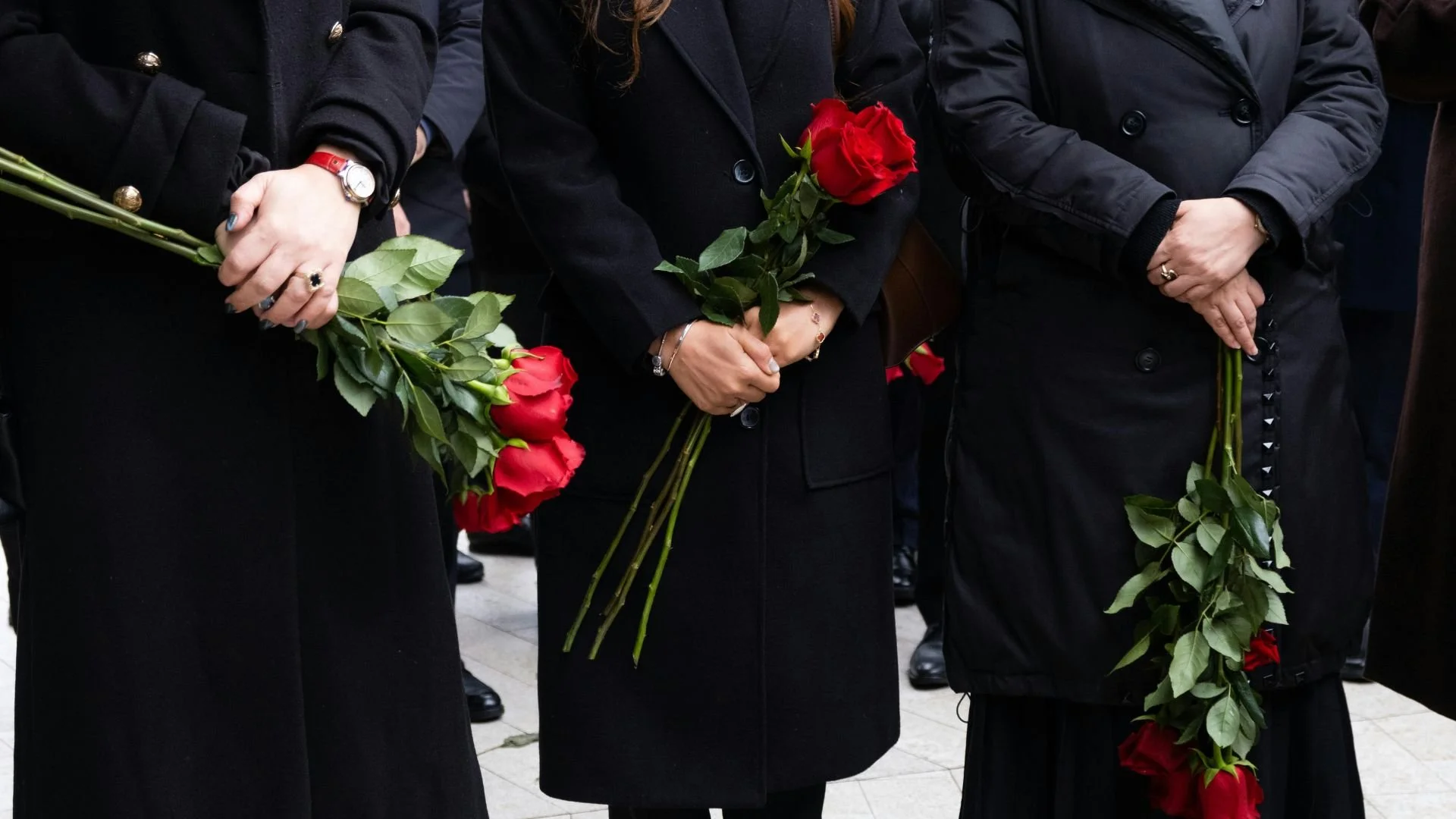 Mourners holding red roses during somber memorial service