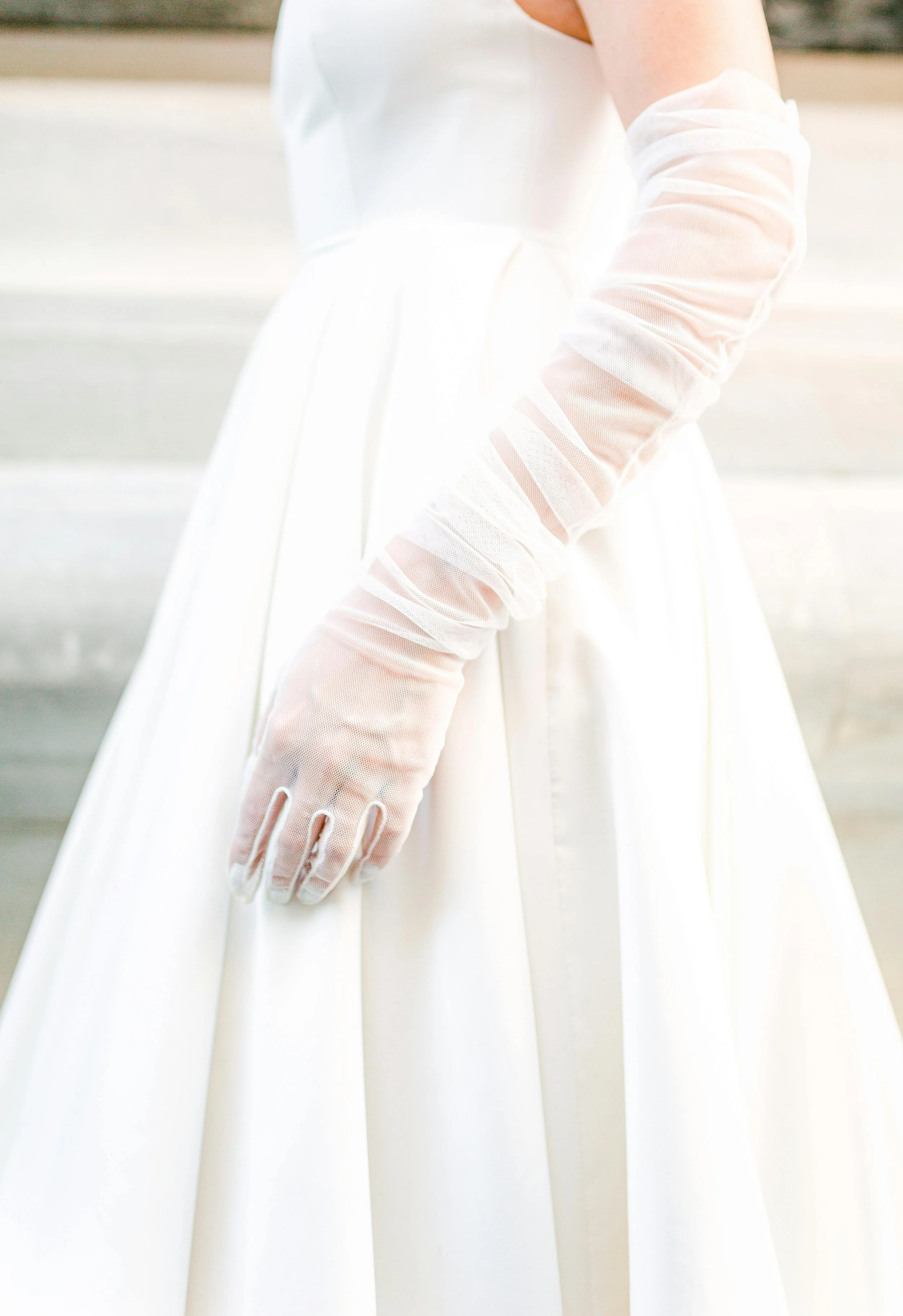 A person wearing a white dress and sheer white gloves.