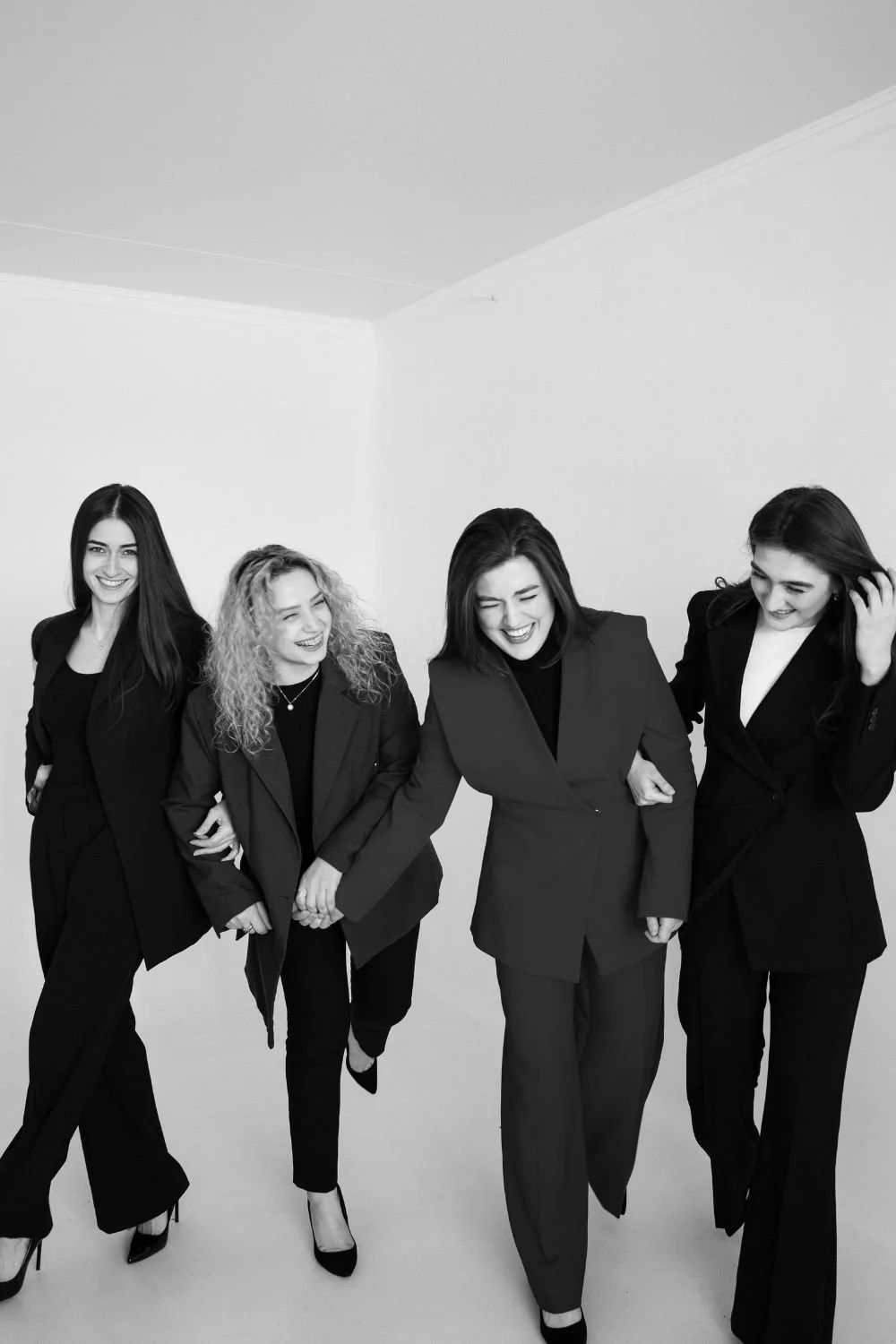 Four women in suits laughing together walking indoors