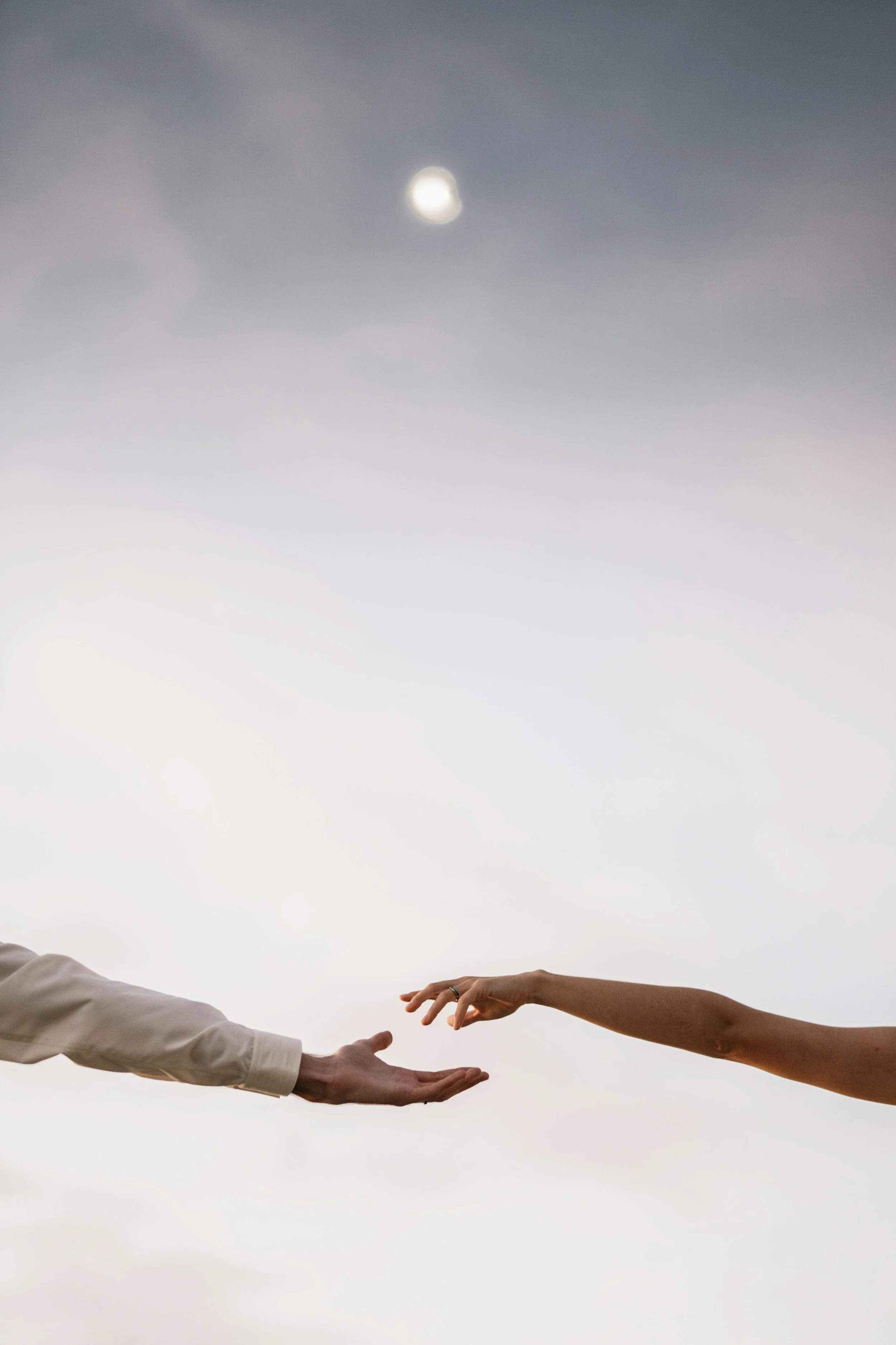 Two hands reaching towards each other against a cloudy sky with the moon visible