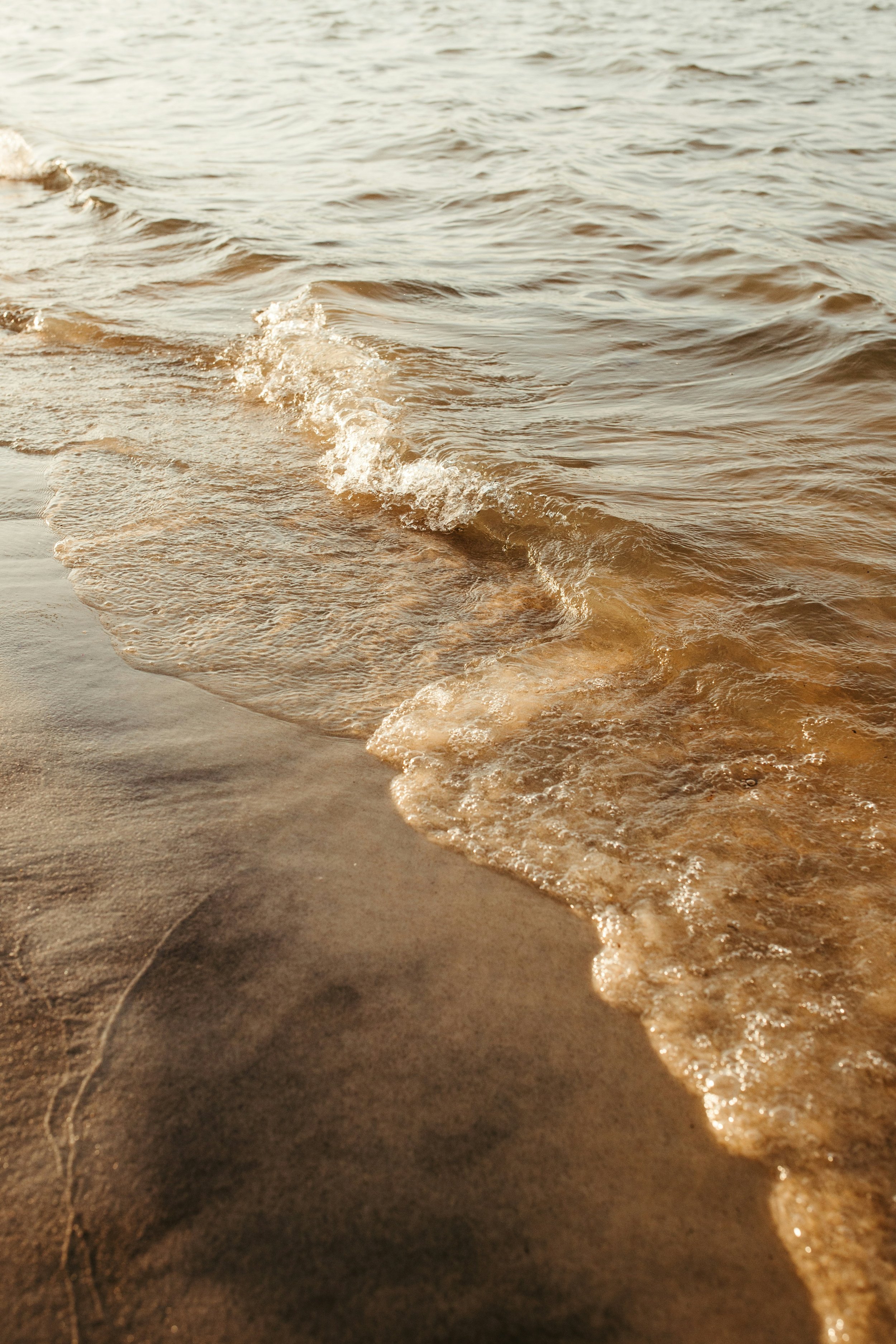 Close-up of gentle waves lapping against a sandy beach, with the water reflecting sunlight.