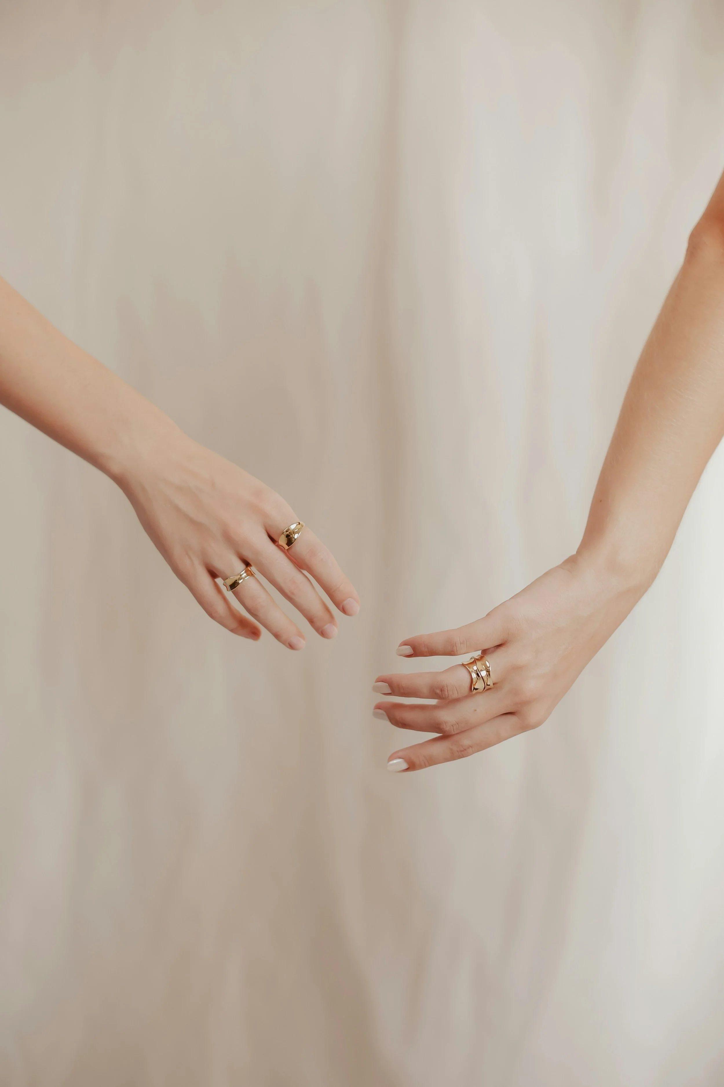 Close-up of two hands reaching towards each other, both wearing multiple gold rings.