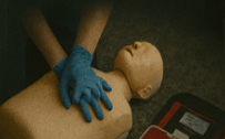Person performing CPR on a mannequin during training, wearing blue gloves.