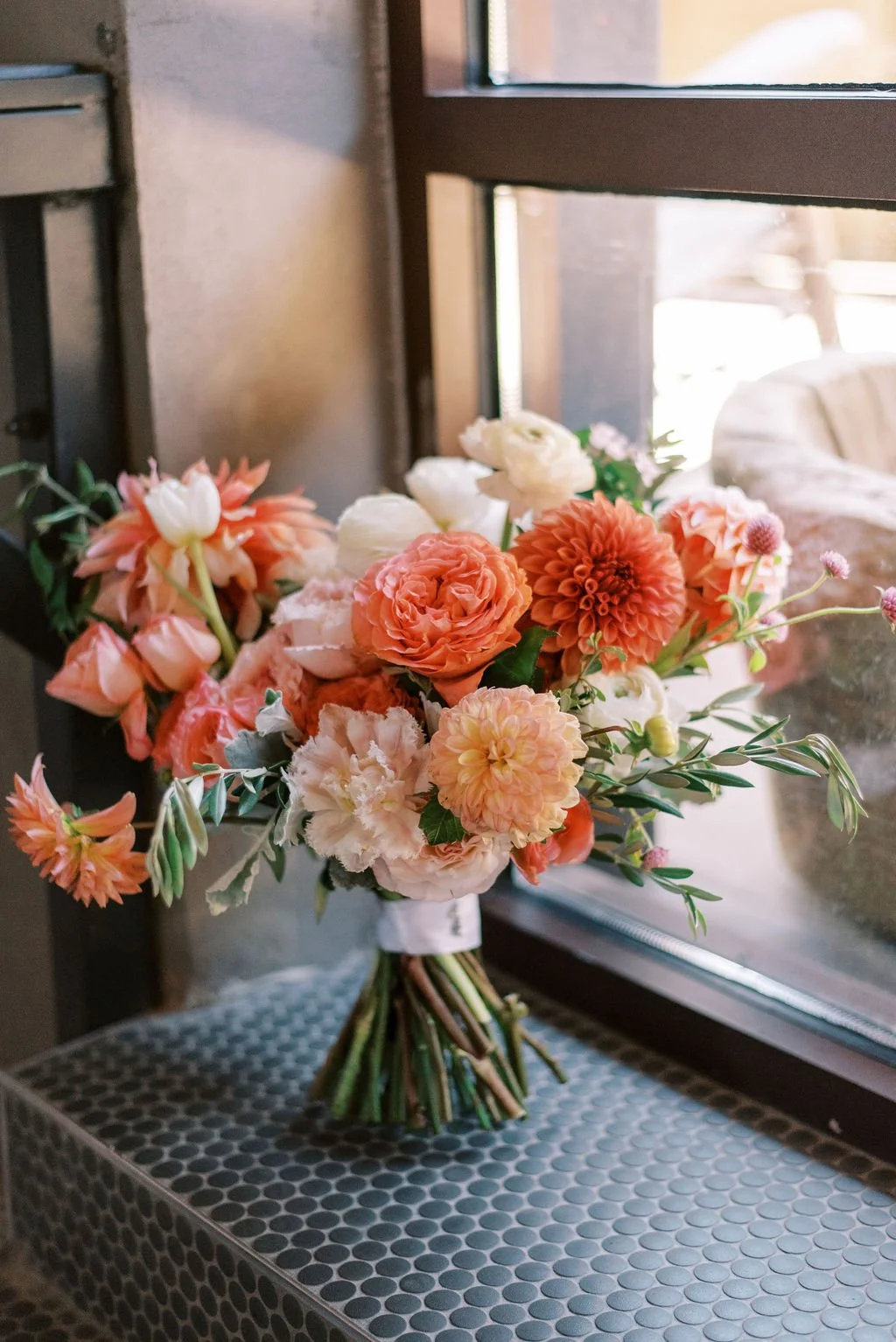 A bouquet of pink, white, and peach flowers on a table near a window.