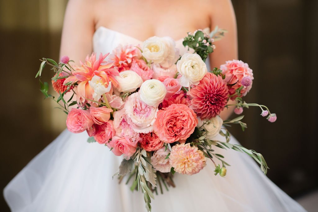 A bride holding a large bouquet of pink and white flowers in front of her white wedding dress.