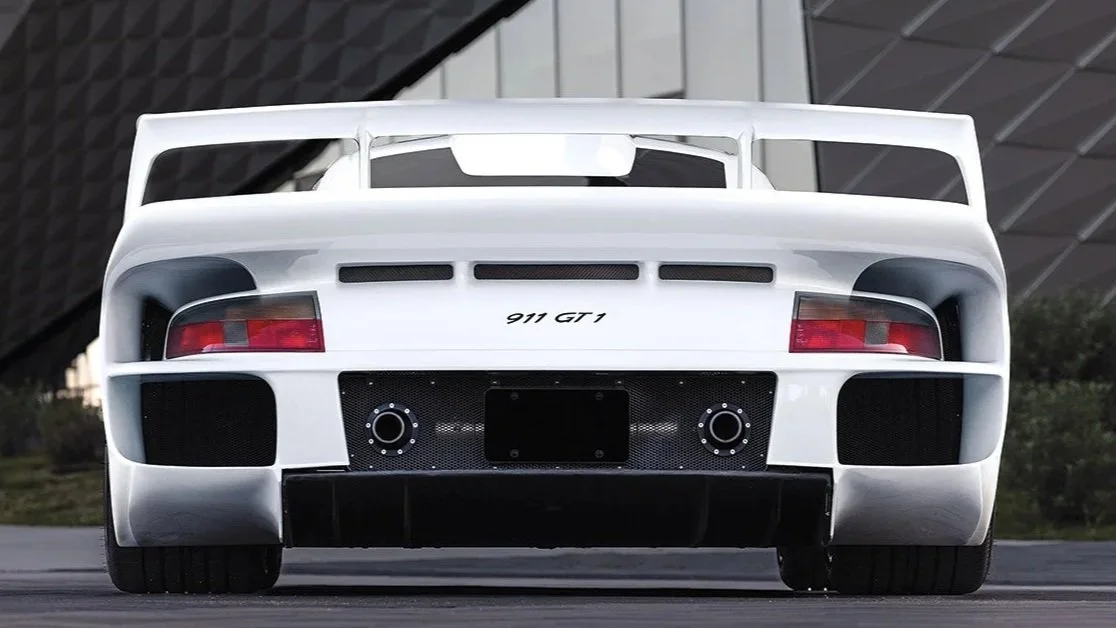 Front view of a white Porsche 911 GT1 sports car parked outdoors with a modern building in the background.