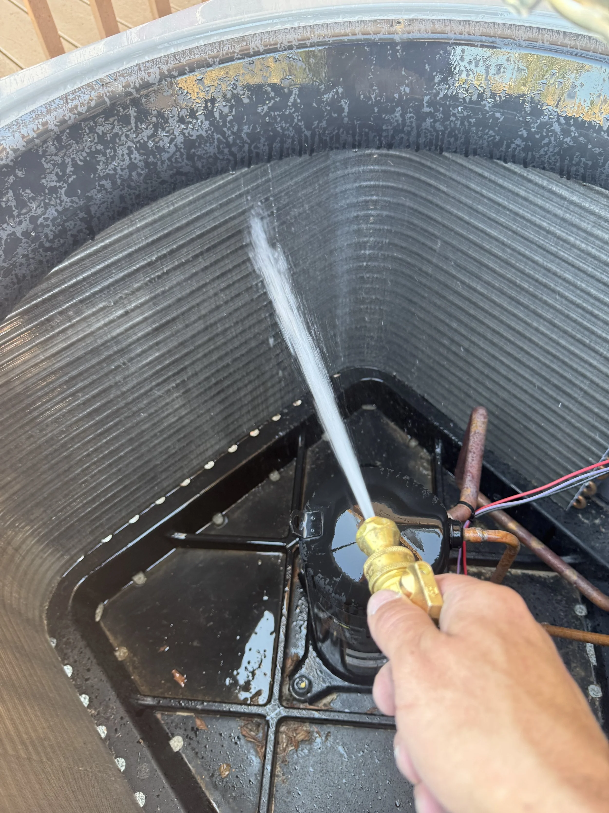 A technician spraying water into the inside of an air conditioner condenser to clean the coils.