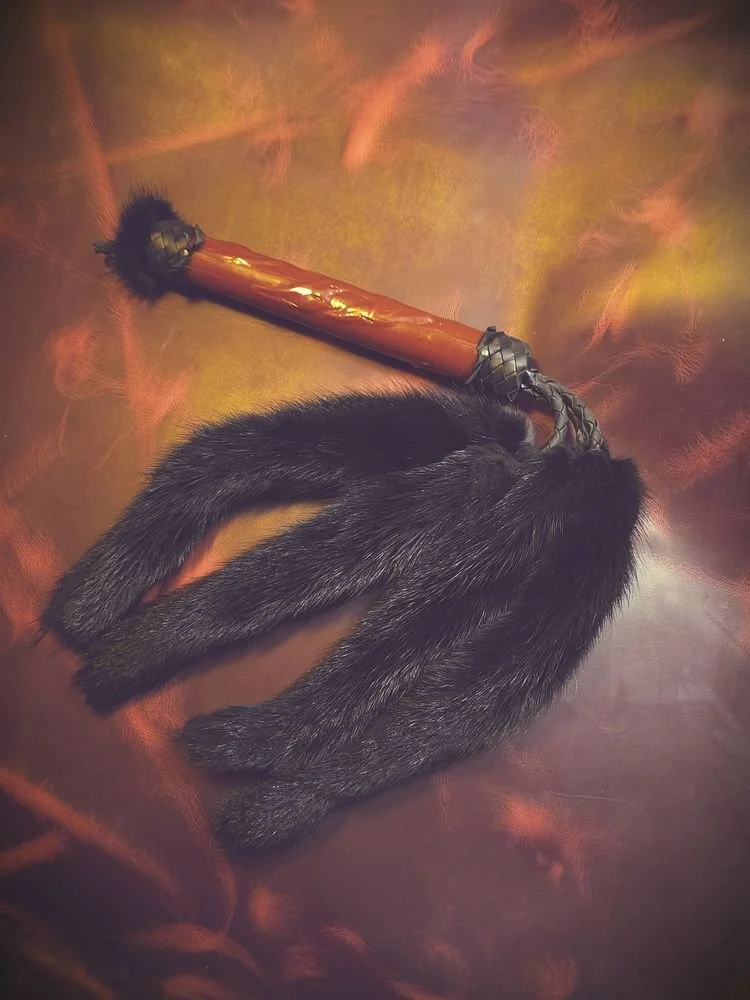 A black rabbit lying on a colorful background with a wooden-handled hammer resting on it.