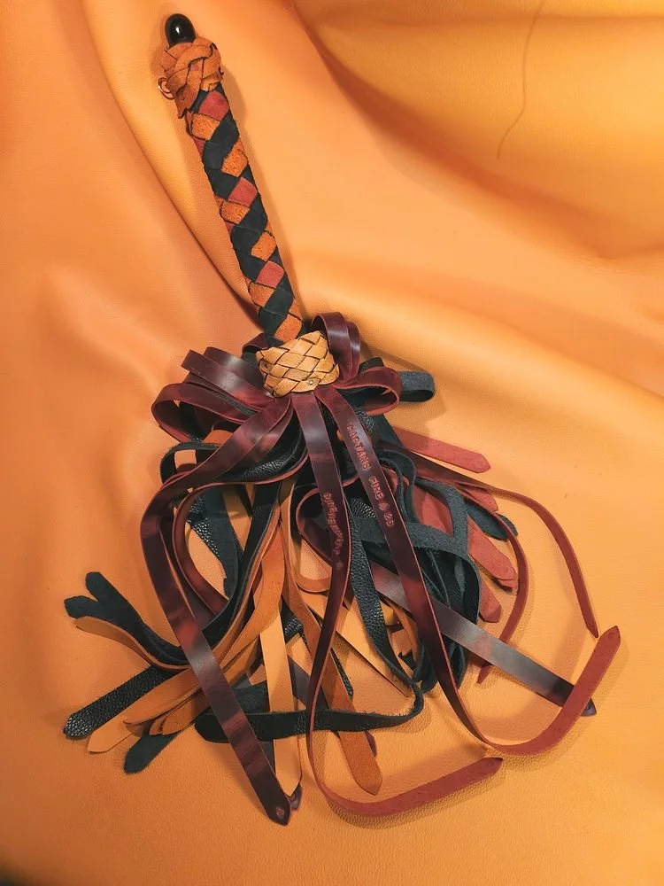 A collection of colorful leather straps and a braided leather handle, arranged on an orange fabric background.