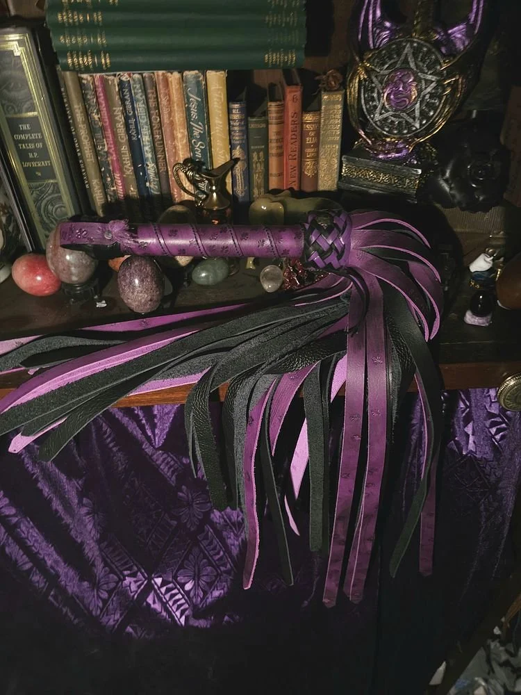 Decorative black and purple feathered accessory with a purple wand handle, placed on a shelf with books, crystals, and mystical items.