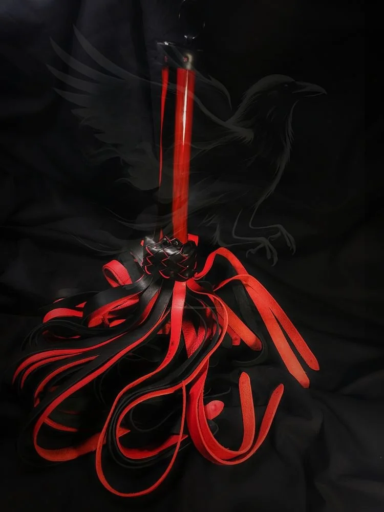 A BDSM flogger with black and red leather strips and a red handle, with a faint outline of a black bird or raven in the background.