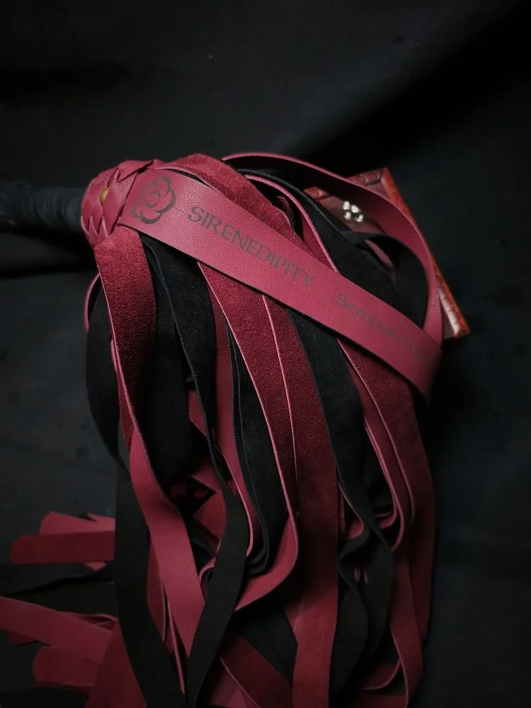 A drumstick with red and black ribbon streamers attached, with the words 'STRENGTH' and 'UNITY' visible on the ribbons.