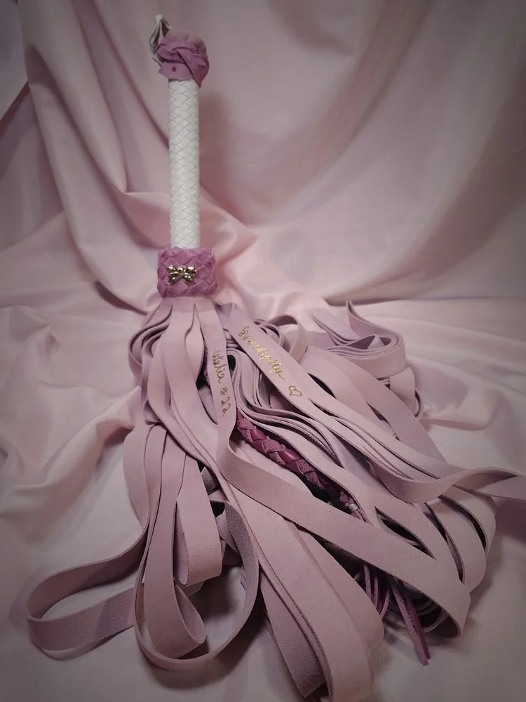 Decorative pink tassel with multiple pink ribbons and a white handle, set against a pink satin fabric background.
