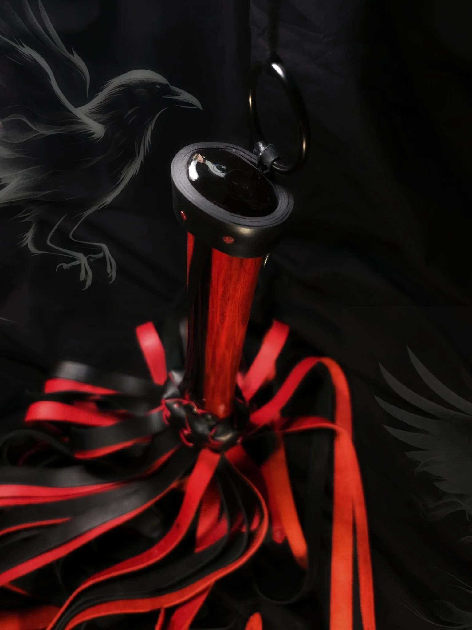 A close-up of a red and black parasol with red ribbons, underneath a black fabric with a white crow illustration.