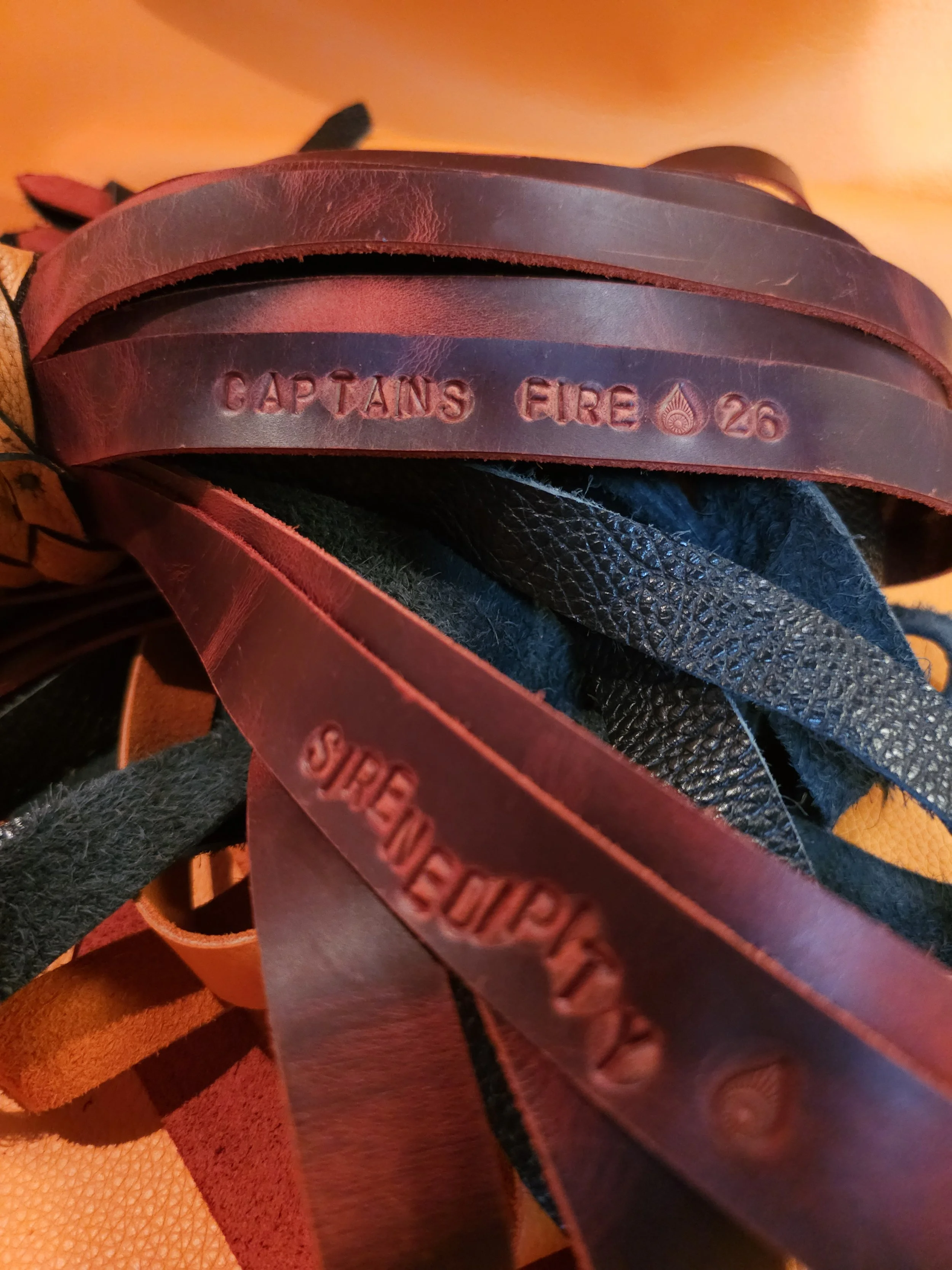 Close-up of leather tags and straps, with one tag reading 'CAPTAINS FIRE' and '26', and another reading 'SURGEWEAR'.