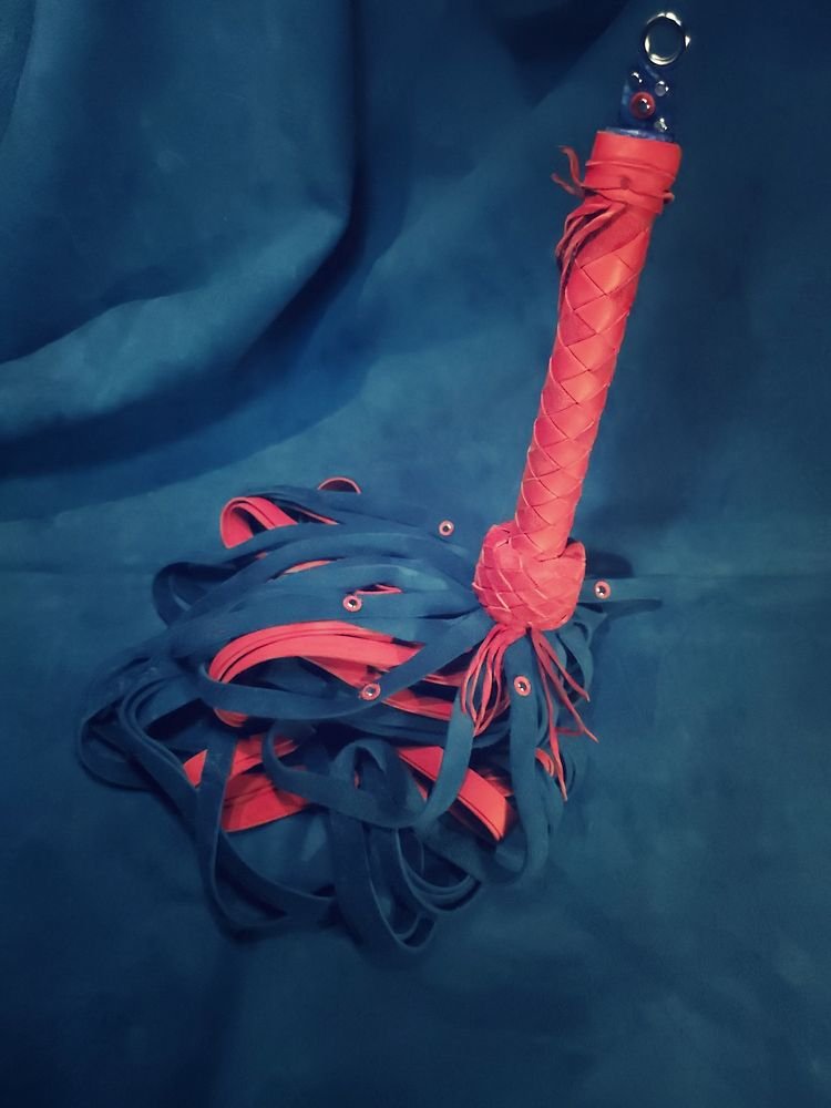 A leash with a padded, braided handle and multiple blue and red fabric strips attached, lying on a blue surface.