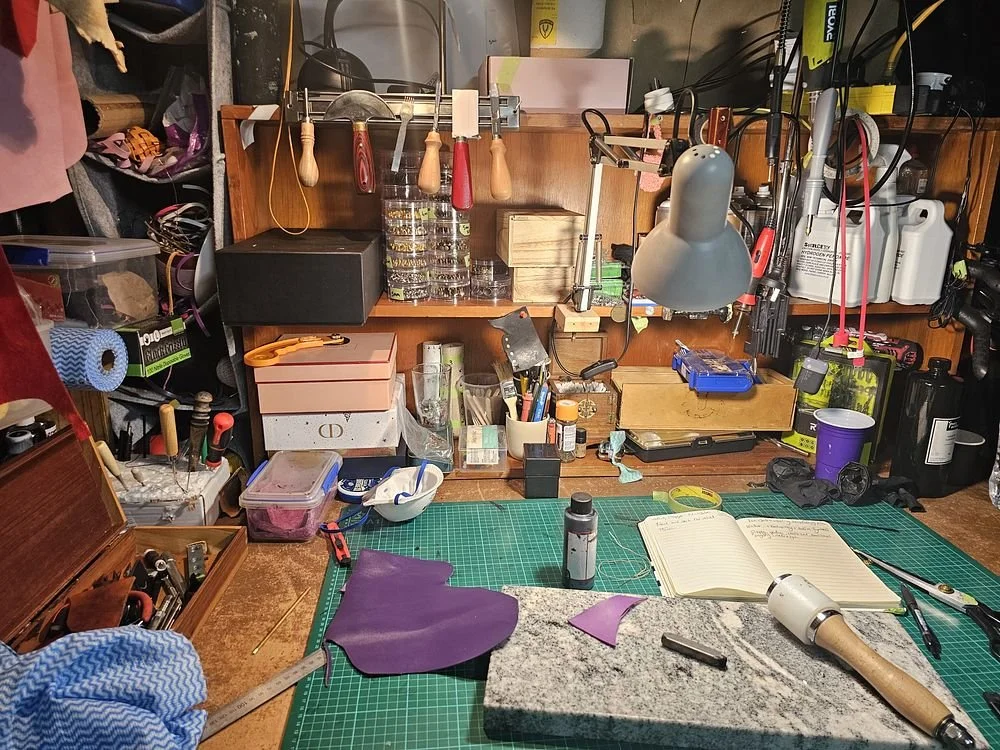 A cluttered woodworking or crafting workspace with various tools, materials, and supplies on a workbench and shelves.