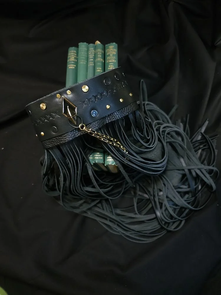 Black leather choker with gold and silver studs, chains, and decorative elements, draped over a set of green hardcover books against a black fabric background.