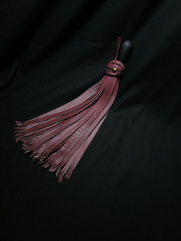 A burgundy leather flogger with multiple strands on a black background.