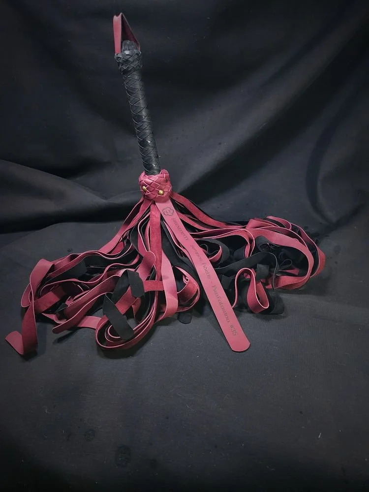 A whip with a braided handle and multiple red and black strips of material hanging from the handle.