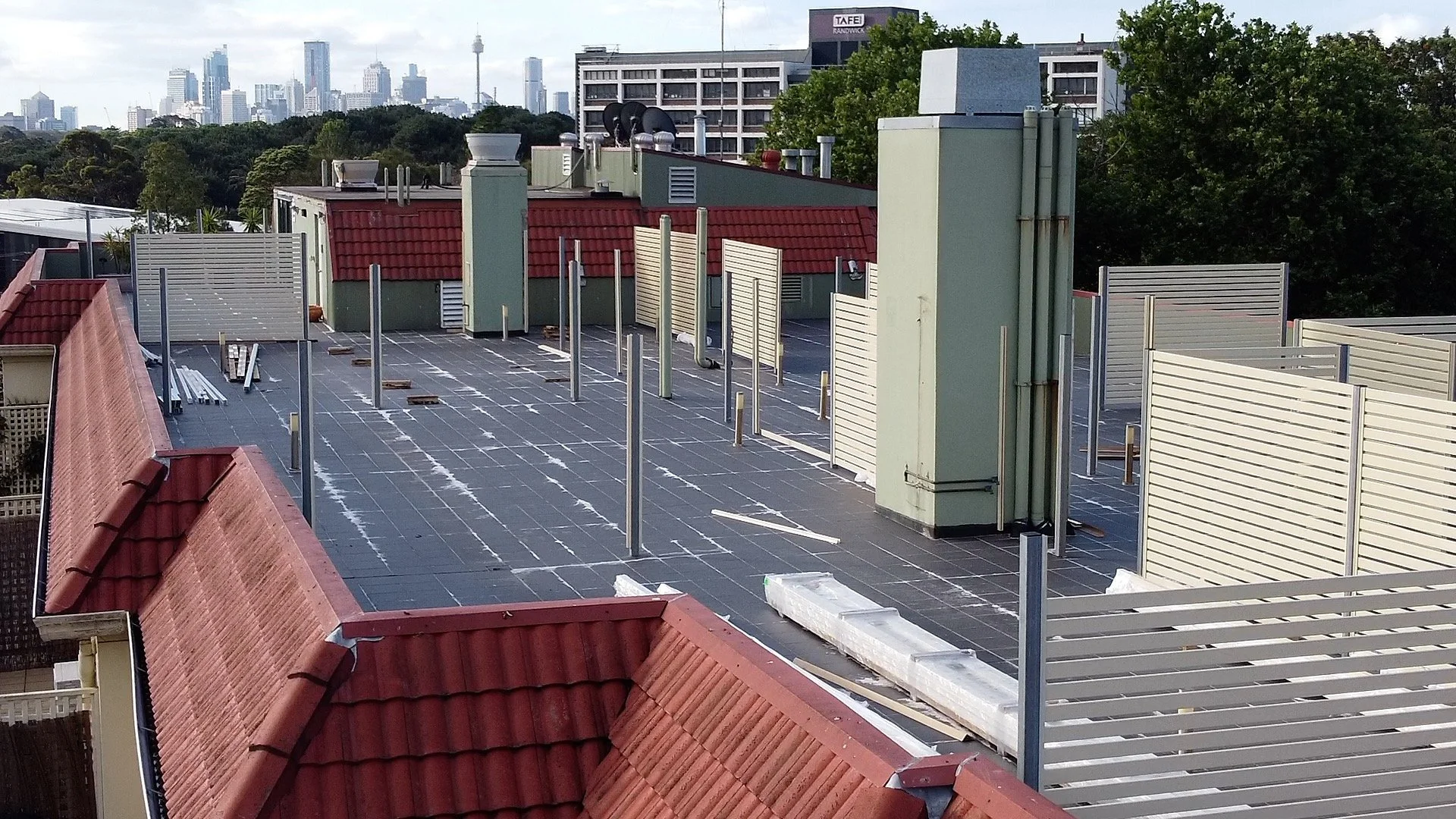 Rooftop terrace under construction with building walls and city skyline in background.