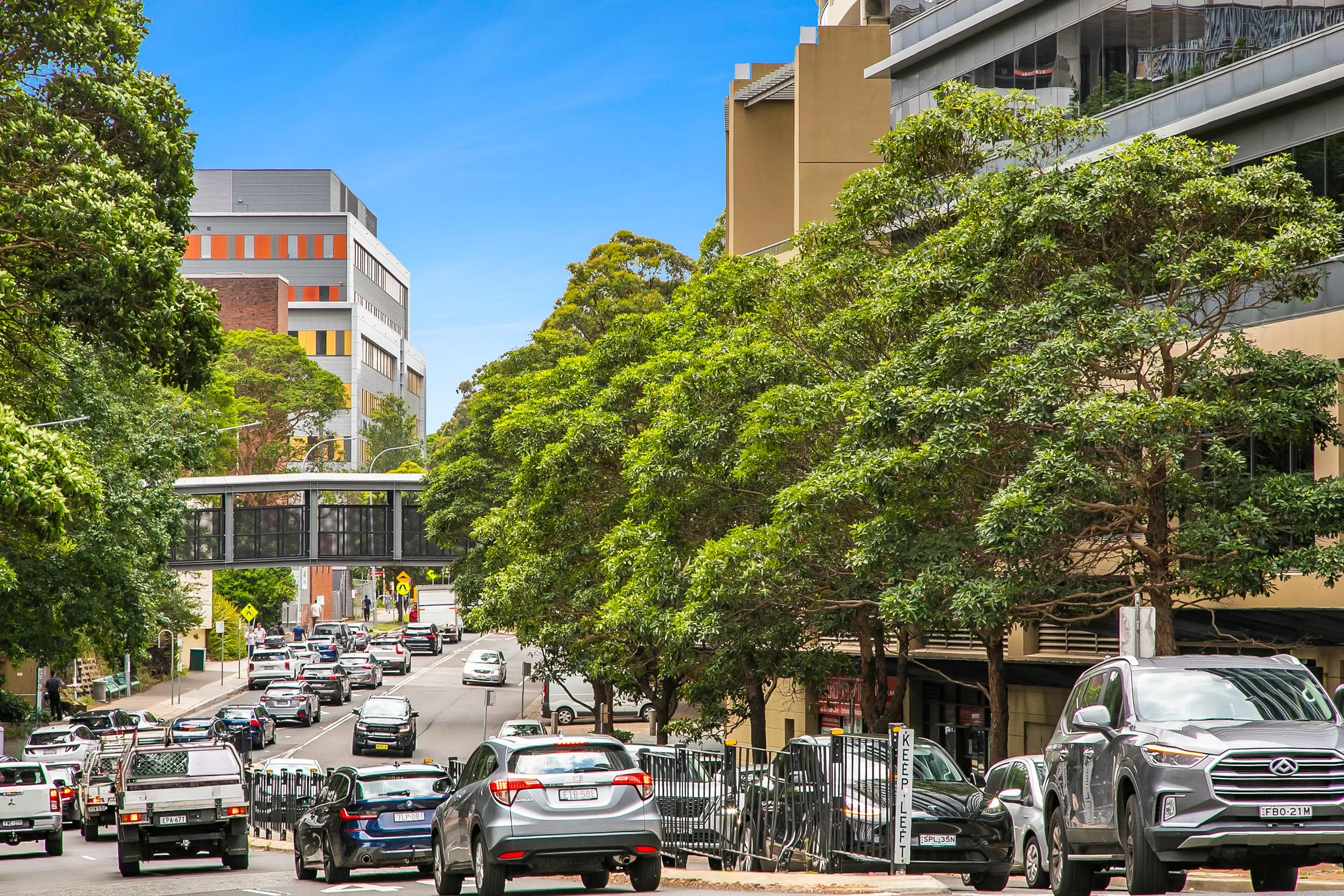 City street corner with cars, showing the footbridge from The Forum to the Royal North Shore Hospital.