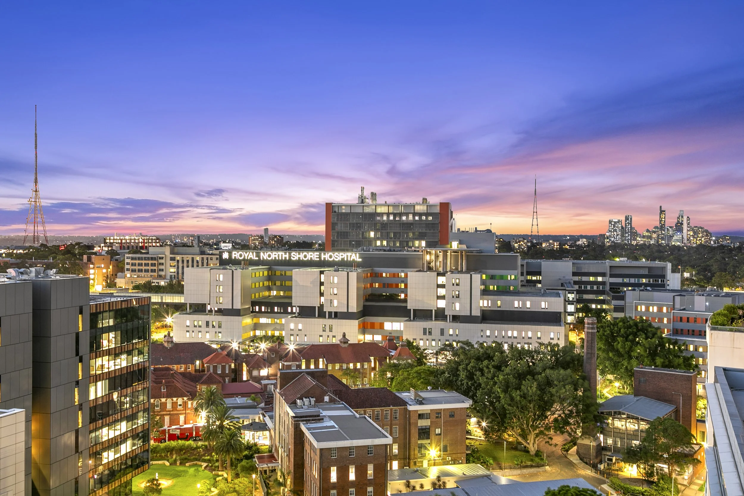 Royal North Shore Hospital building, trees, and a sunset sky with purple and pink clouds.