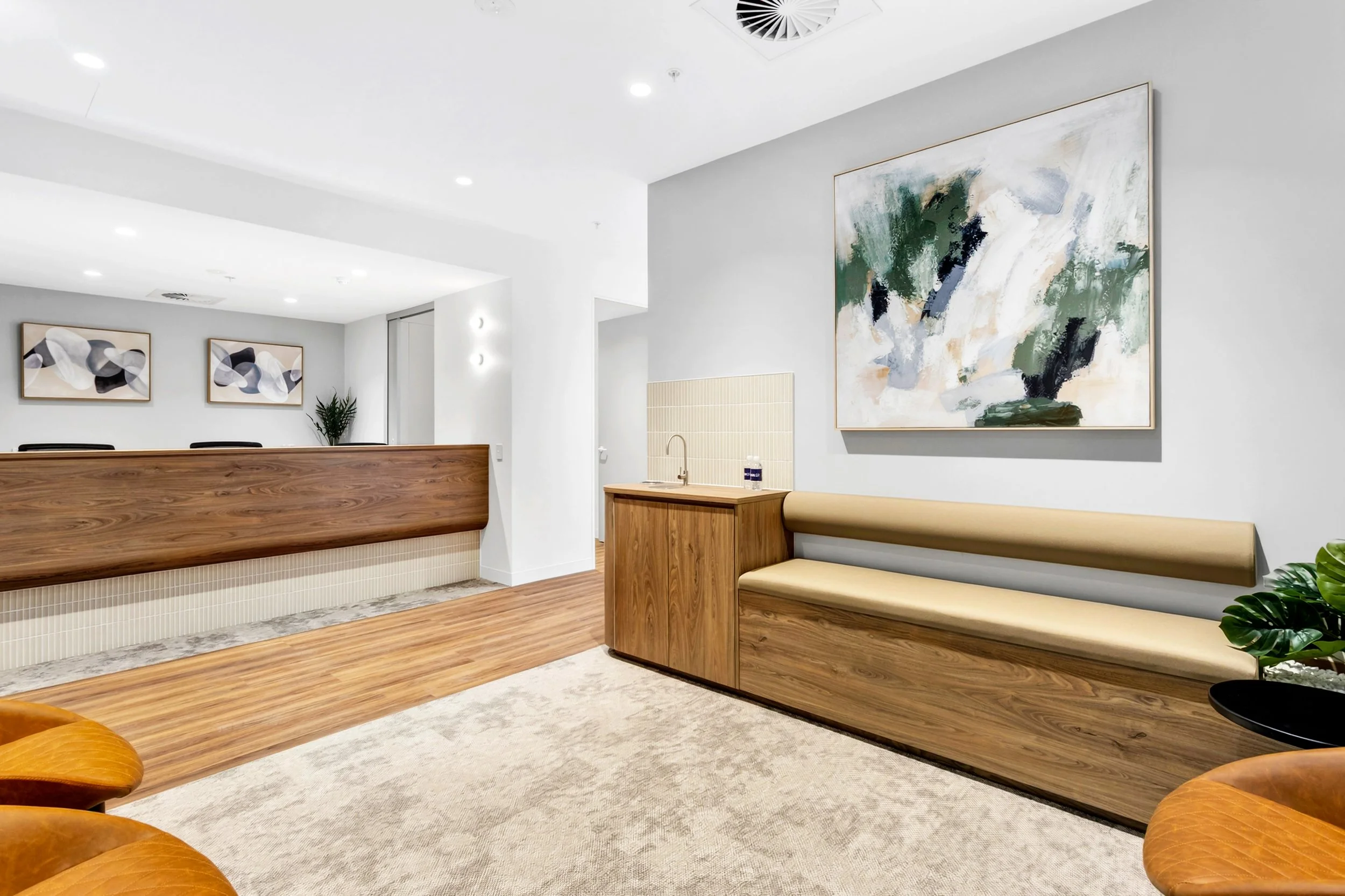 Modern interior of a waiting area with wooden countertops, beige seating bench, abstract wall art, and potted plants.
