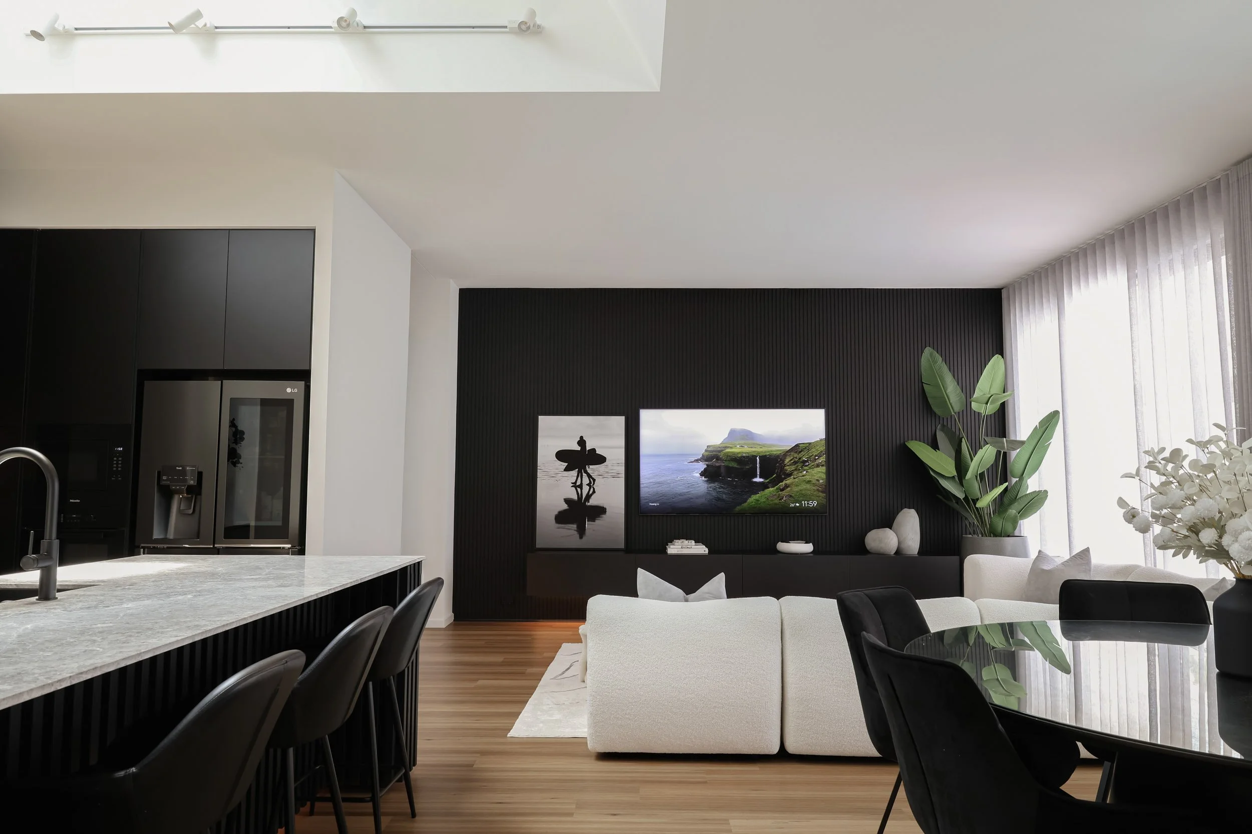 Modern open plan living with a view of the kitchen lounge room and dining room with feature chambered grey limestone bench top and black timber feature wall panelling