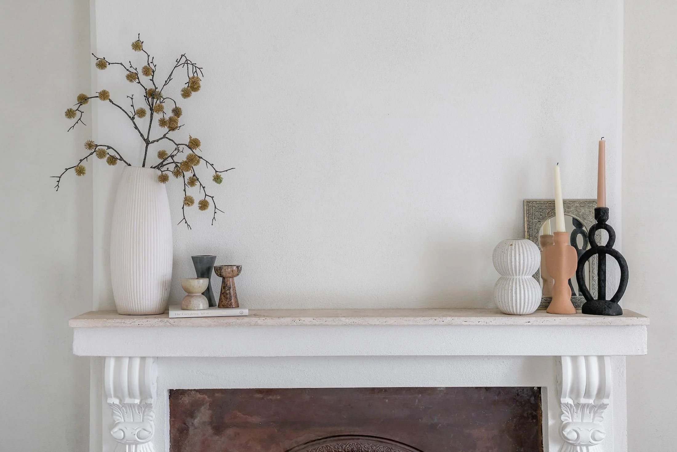 Decorative mantelpiece with vases, candles, and framed artwork against a white wall.