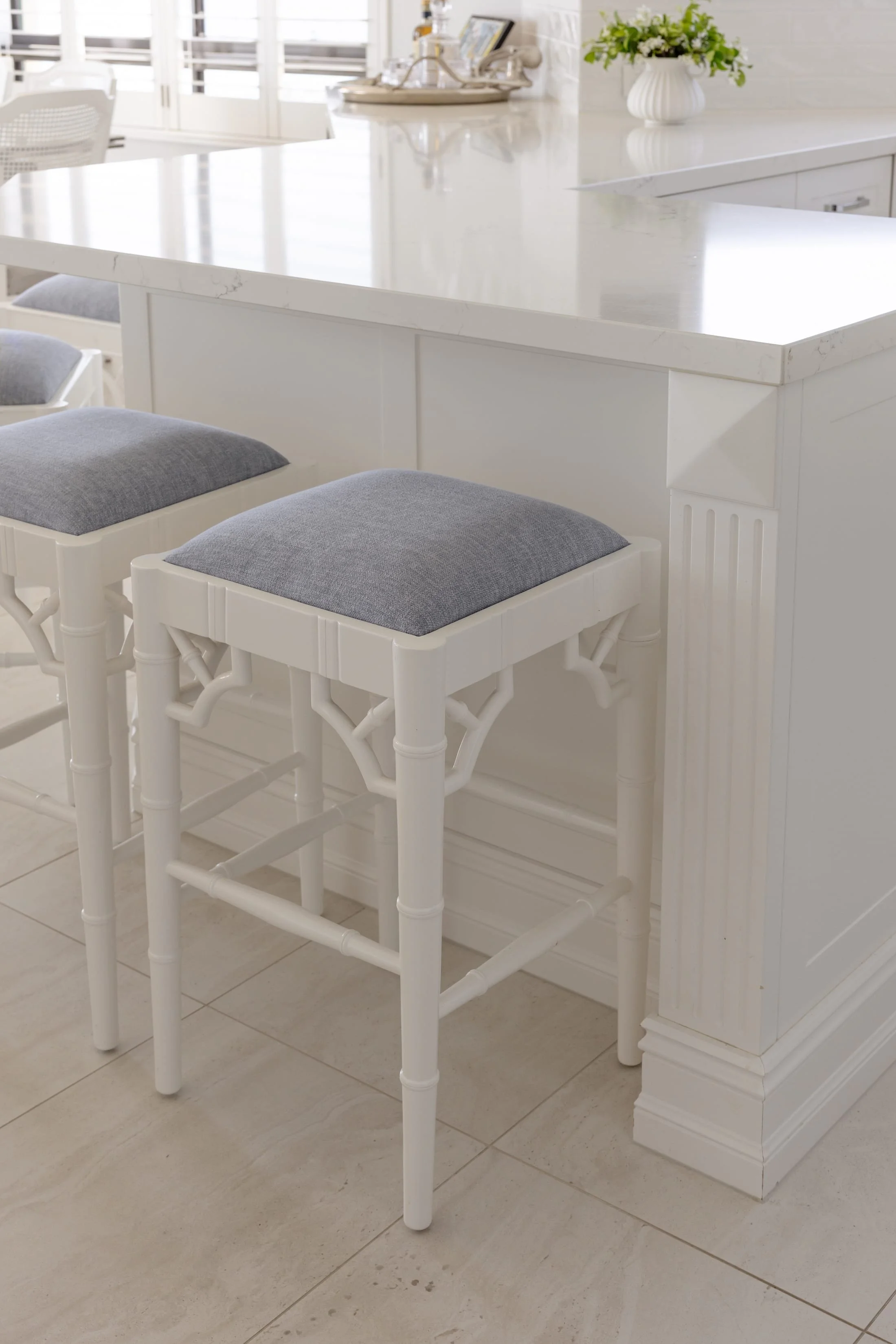 White kitchen island with a marble countertop, three gray-cushioned bar stools, and a potted plant on the counter.