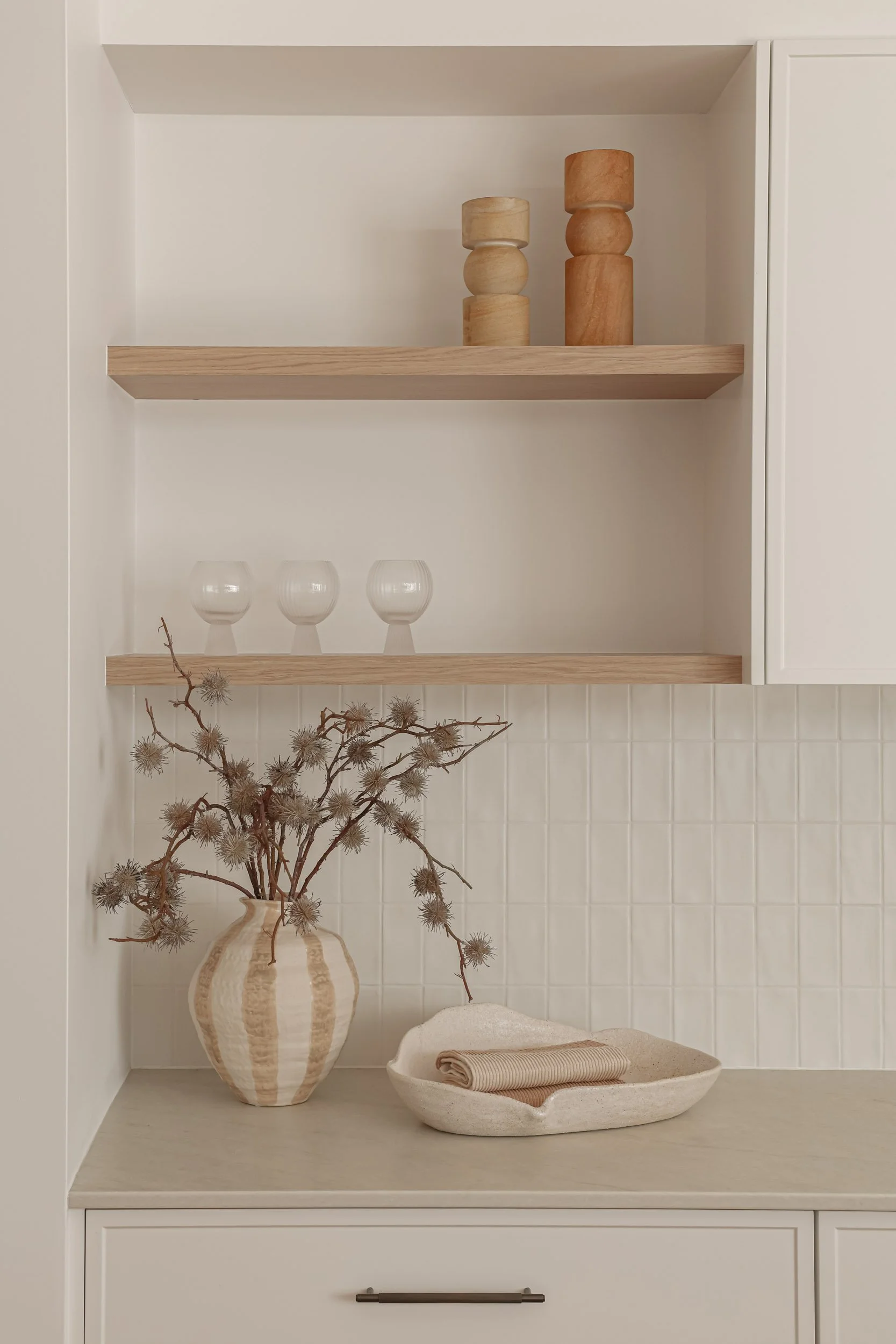 open timber shelving, taj mahal stone, slim shaker cabinetry, timber styling pieces, neutral string pieces, antique brass handle, off white wall paint, white feature tile, 3 glasses