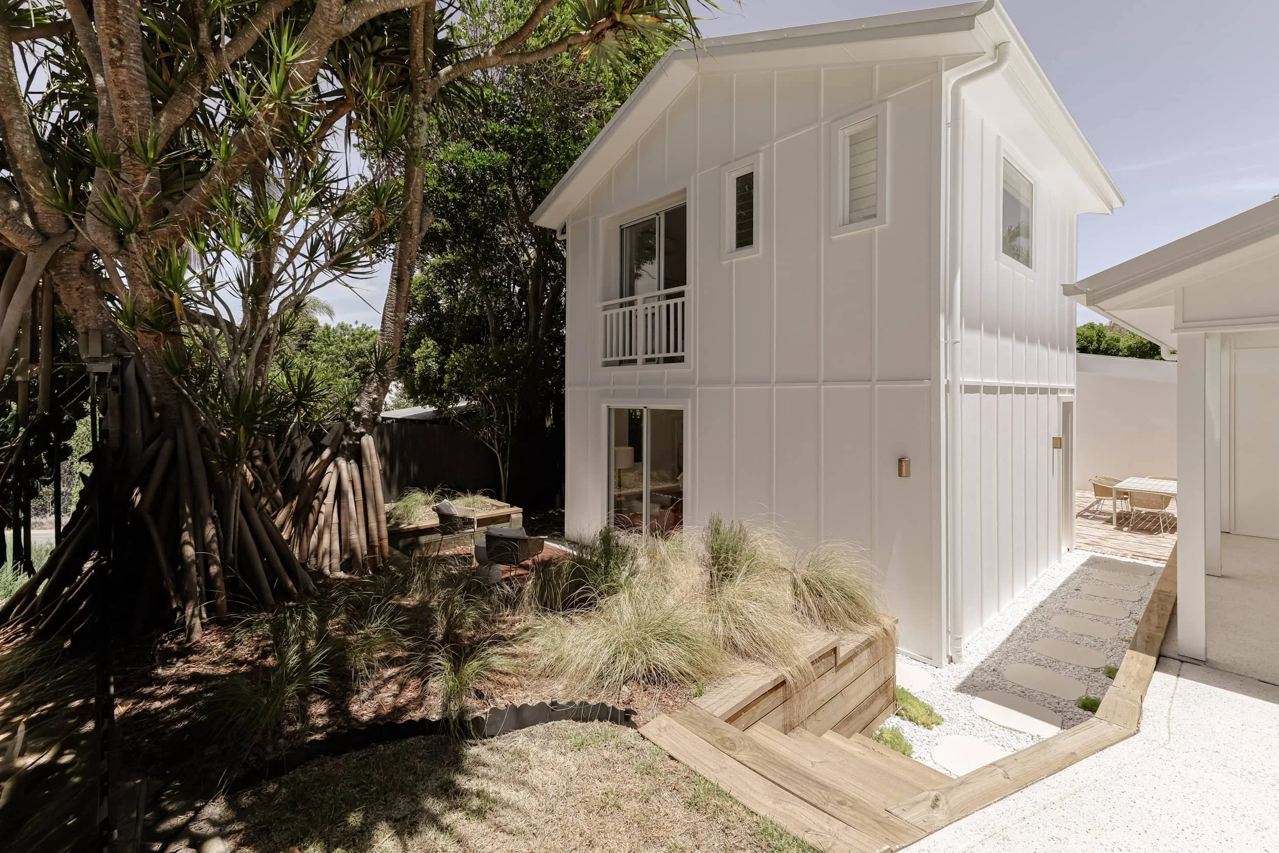 Pandanus tree, white claw exterior, antique brass exterior light, timber retaining wall and stairs, white pebbles and steppers, grass plants, juliette balcony, white exterior windows, white rood, white undercover carport, modern coastal
