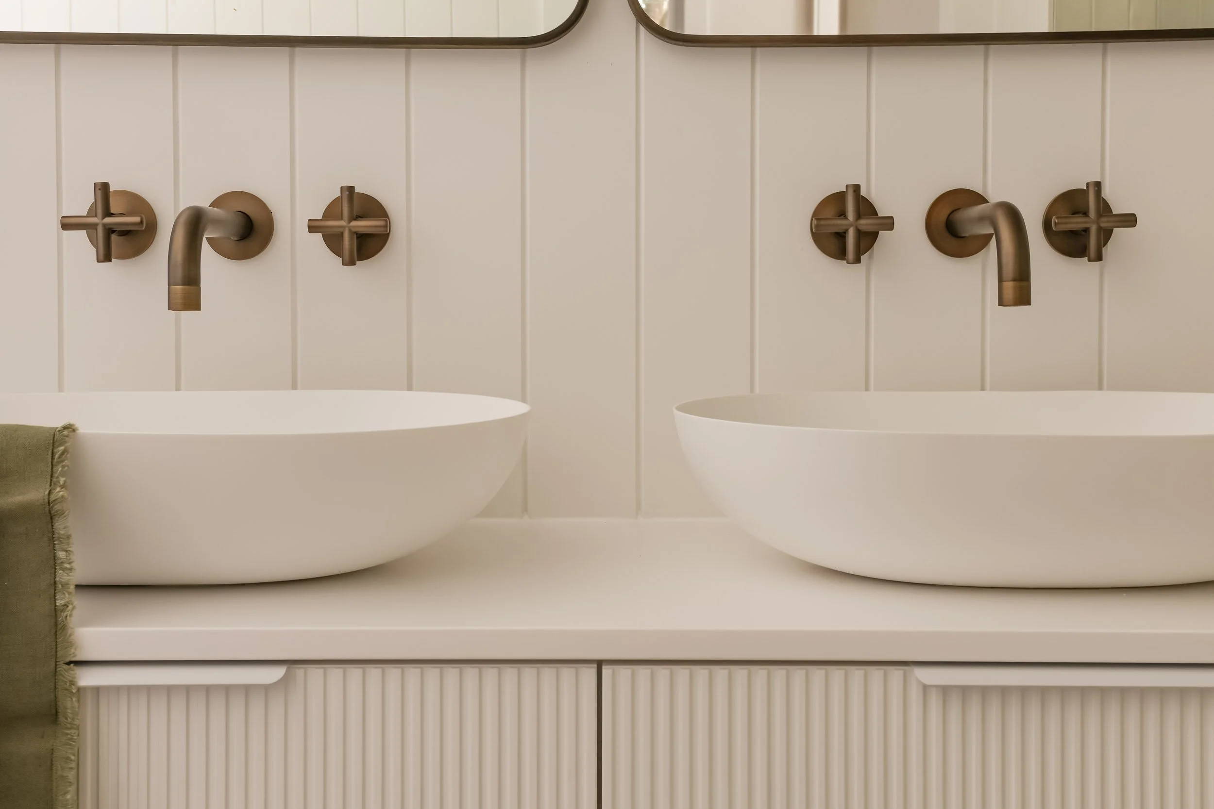 Antique brass mirrors, antique brass tapware, white fluted vanity, white stone bench top, green linen hand towel, white VJ wall panelling, white cabinet handles