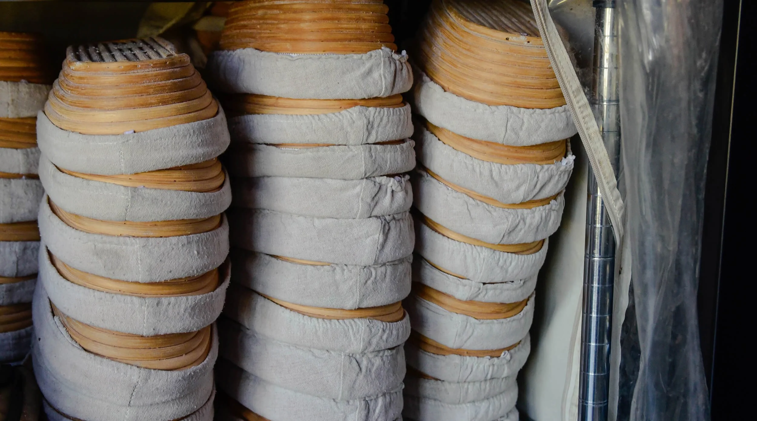 Stacks of round, woven bamboo steamers with cloth liners, stored against a wall.