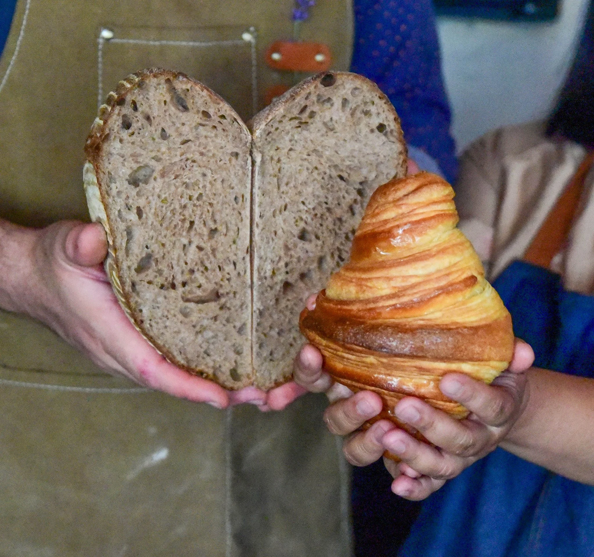 Two hands holding a slice of multigrain bread and a croissant.
