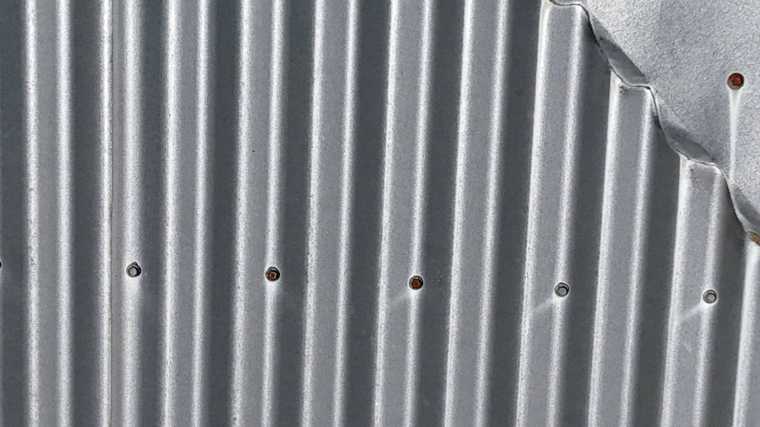 Close-up of a corrugated metal surface with some rusty screws.