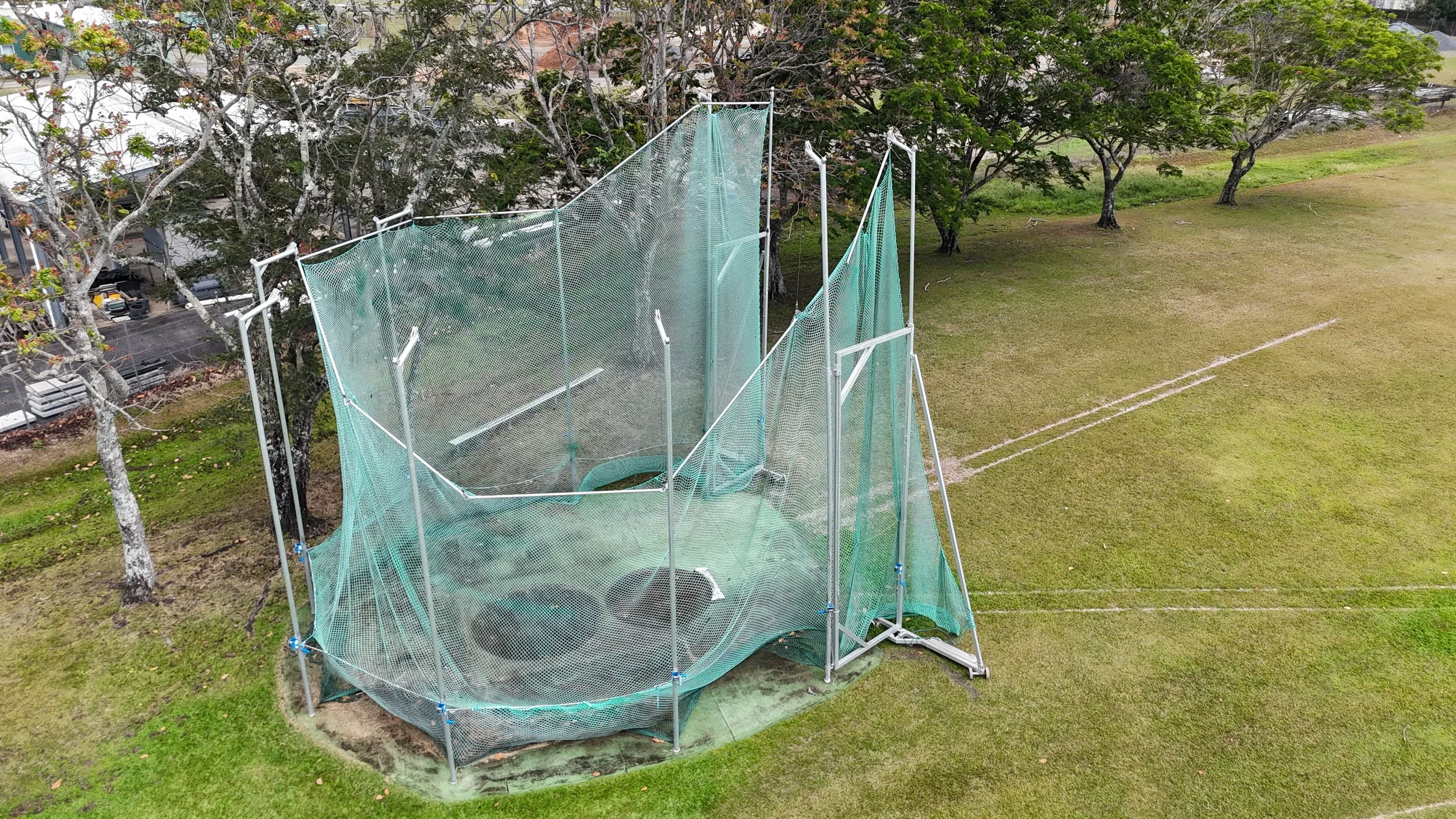 An outdoor sports facility enclosed by green safety netting, set on a grassy field with trees nearby.