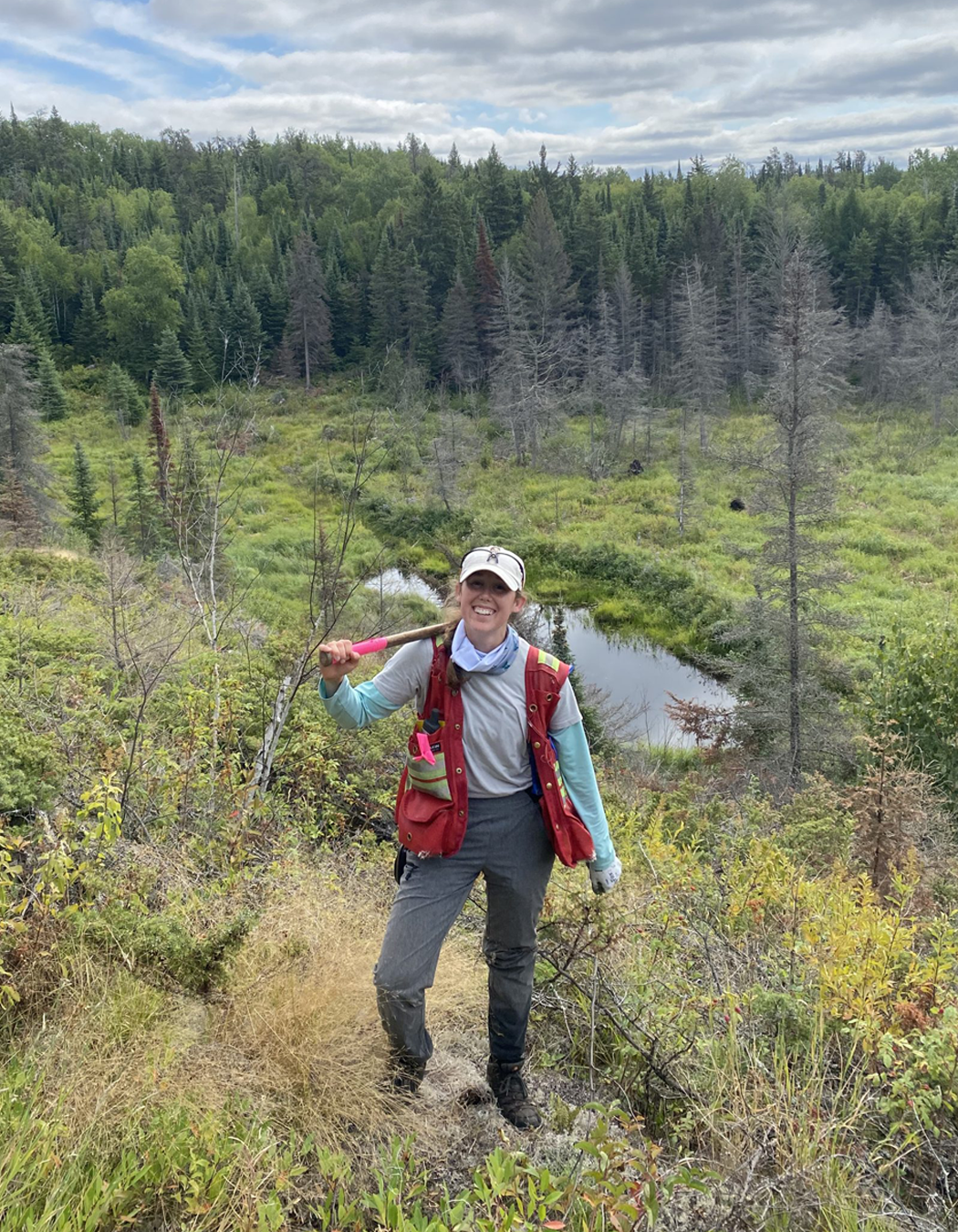 A woman hiking in a lush forested area with a creek and trees in the background.