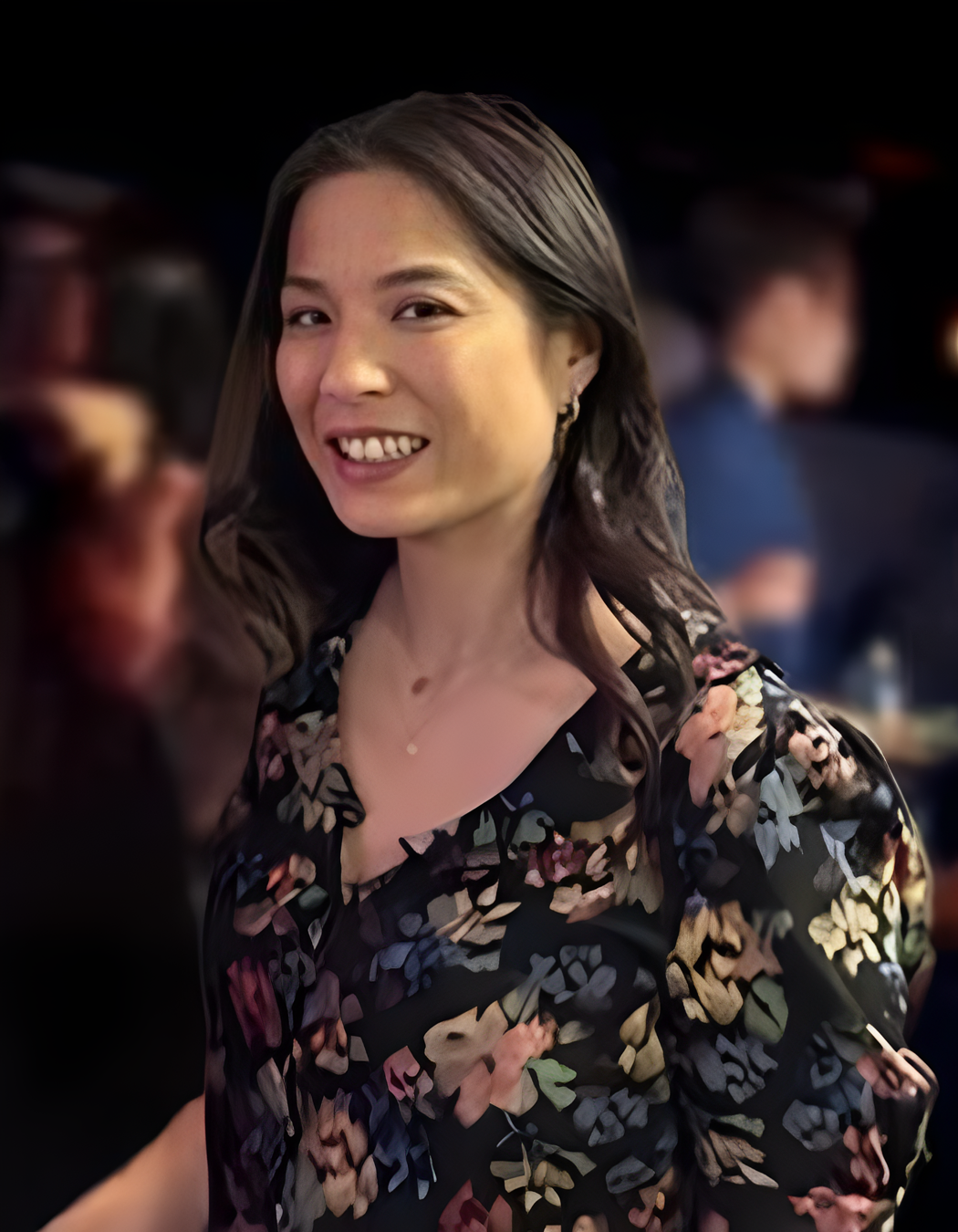 A woman smiling at a social gathering, wearing a floral patterned top with earrings.