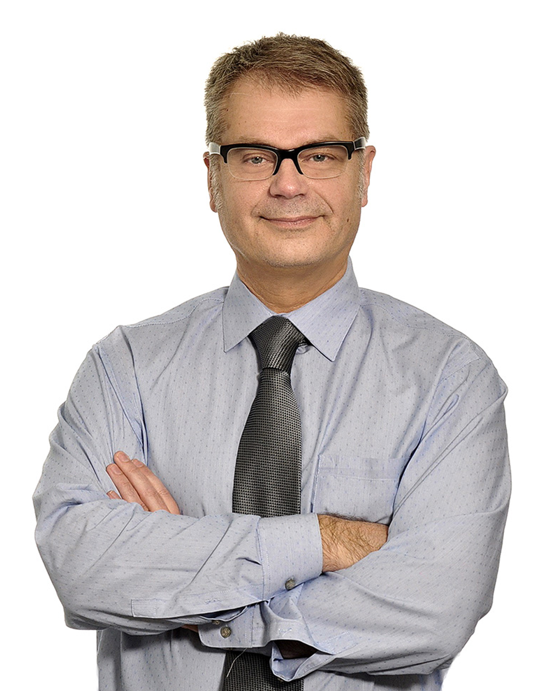 A middle-aged man with glasses, wearing a light blue dress shirt and a dark gray tie, standing with arms crossed against a white background.
