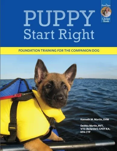 An image of the Puppy Start Right book featuring a small Malinois puppy in a yellow life jacket on an inflatable kayak on a river.