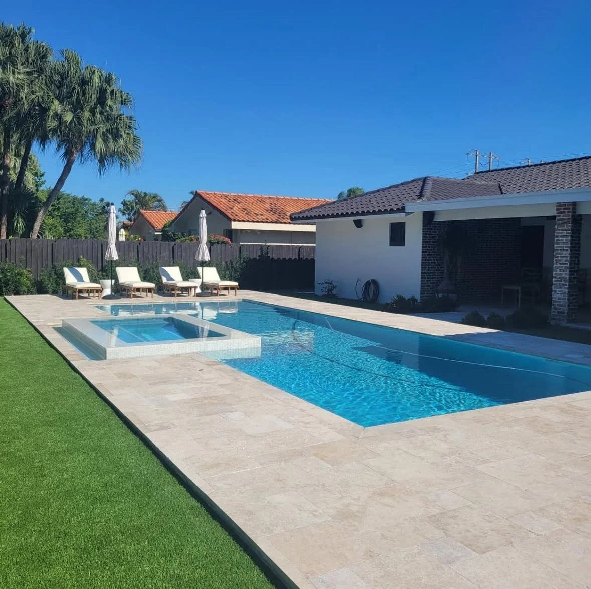 A backyard with a swimming pool, hot tub, and lounge chairs with umbrellas on a sunny day.