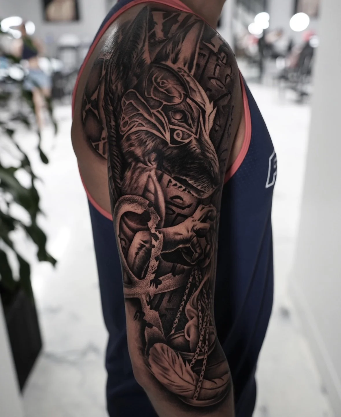 Close-up of a person's arm with a detailed black and gray tattoo featuring a wolf wearing a horned helmet, surrounded by chains and abstract designs.