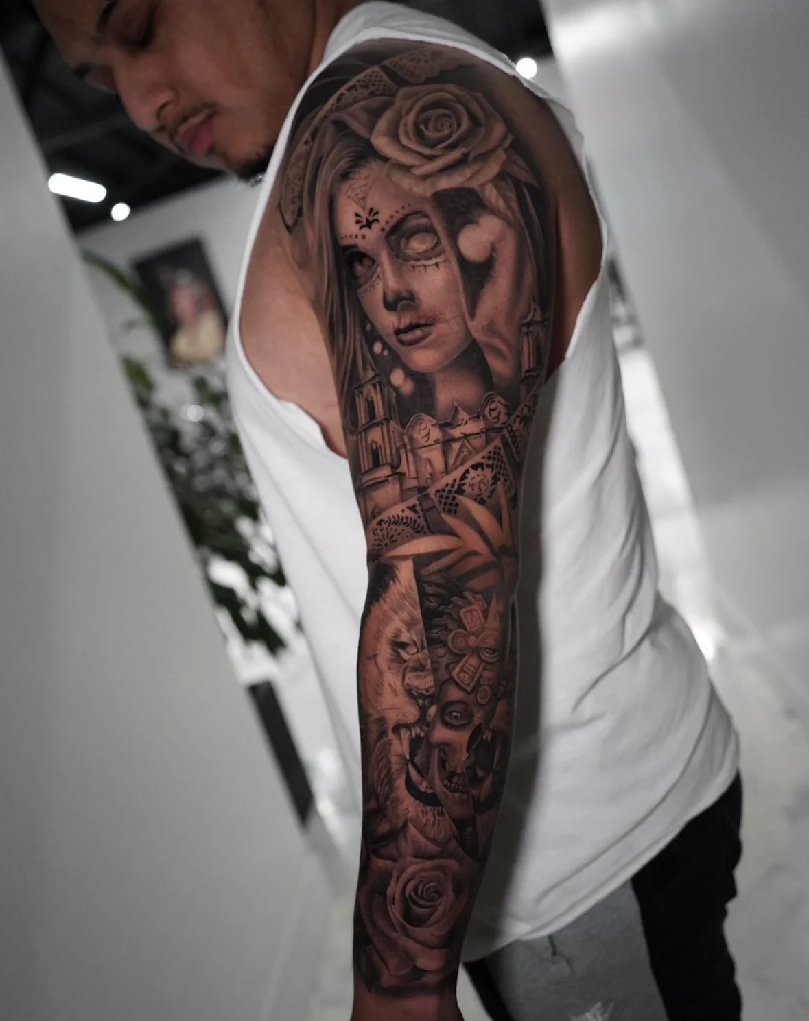 Tattoo sleeve featuring a woman's face, a lion, a skull, roses, and various decorative elements on a man's arm.